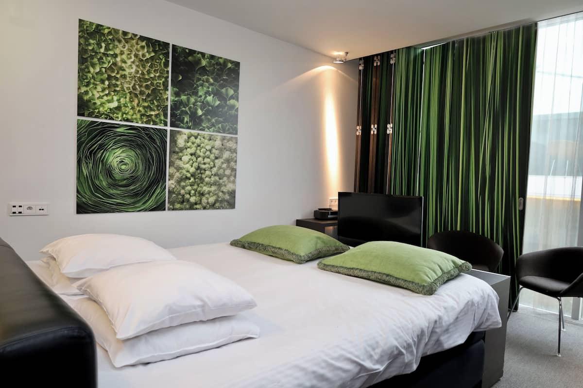 A modern hotel room with a large bed, two green pillows, a flat-screen TV, a desk, and a chair.