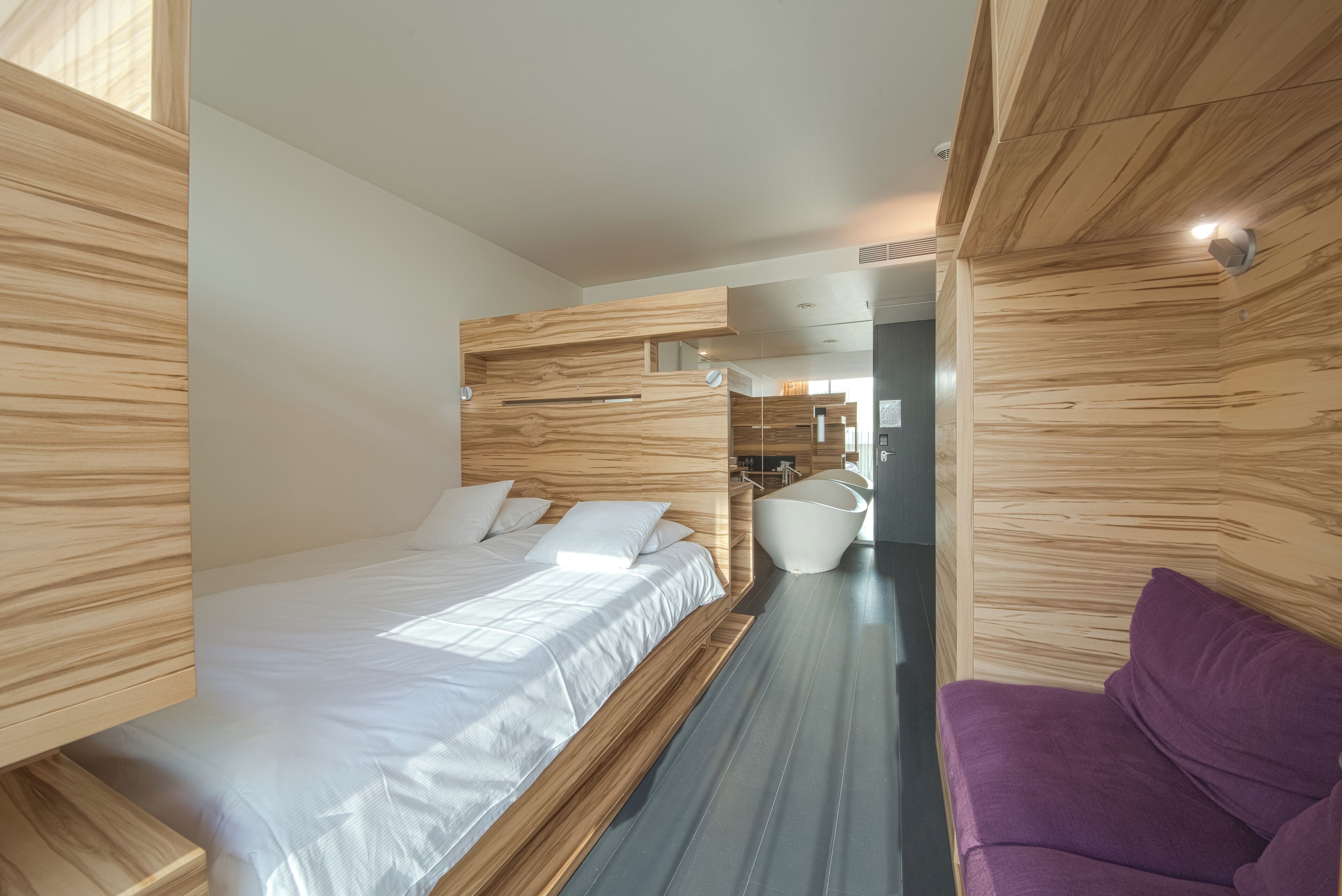A modern bedroom with a wooden headboard, a large bed, a purple sofa, and a built-in white cabinet.