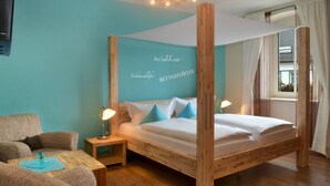 A bedroom with a wooden four-poster bed, a small bedside table with a lamp, a sofa, and a wall with text. - Gasthof Deutscher Adler & Hotel Puchtler (Bischofsgruen)