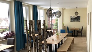 A dining area with wooden tables and benches, blue chairs, and a view of the outdoors through large windows. - Gasthof Deutscher Adler & Hotel Puchtler (Bischofsgruen)