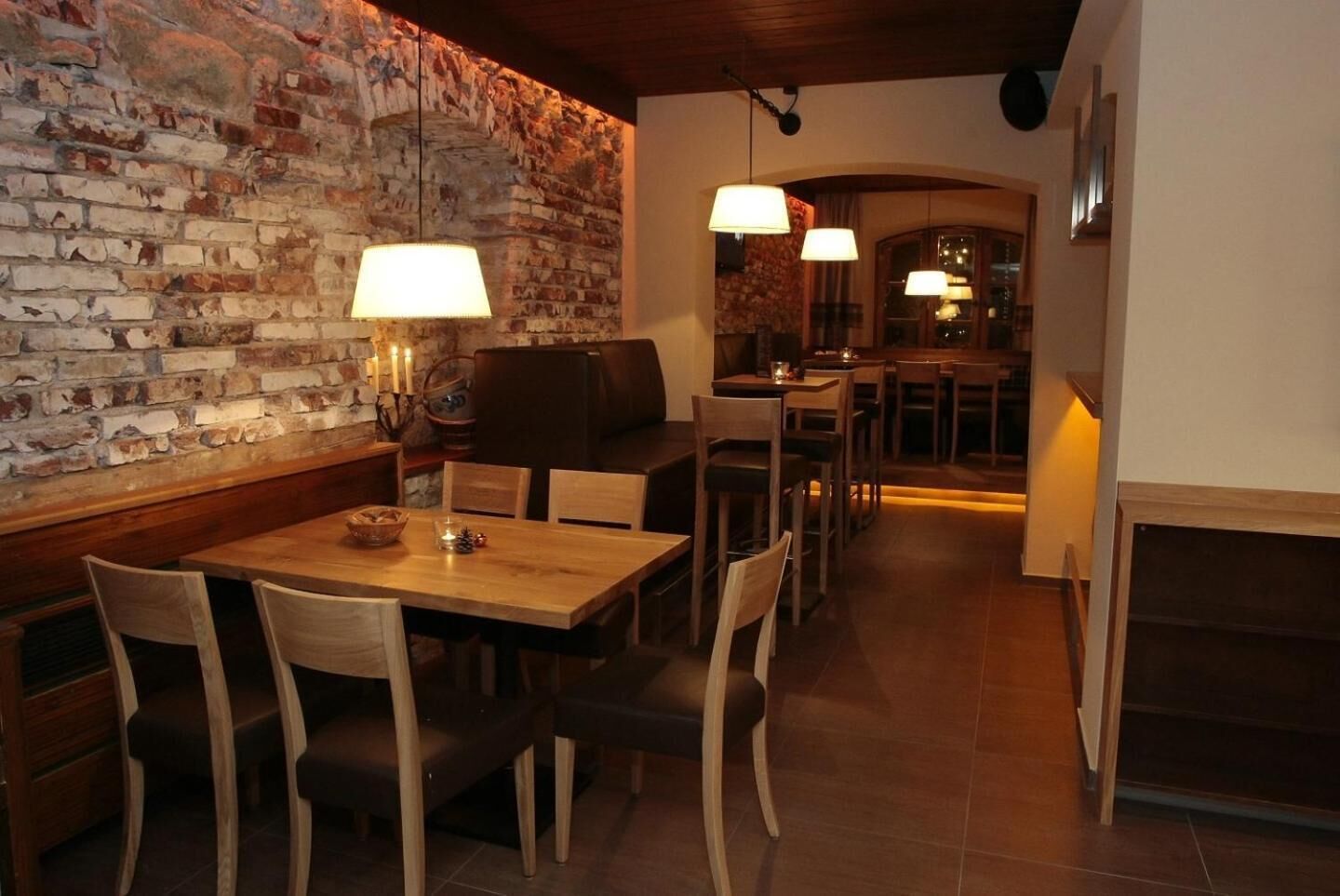 A cozy restaurant with a brick wall, wooden tables, and chairs. There are hanging lamps and a fireplace.