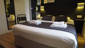 A modern hotel room with a large bed, a bedside table, a mirror, and wall-mounted lighting.