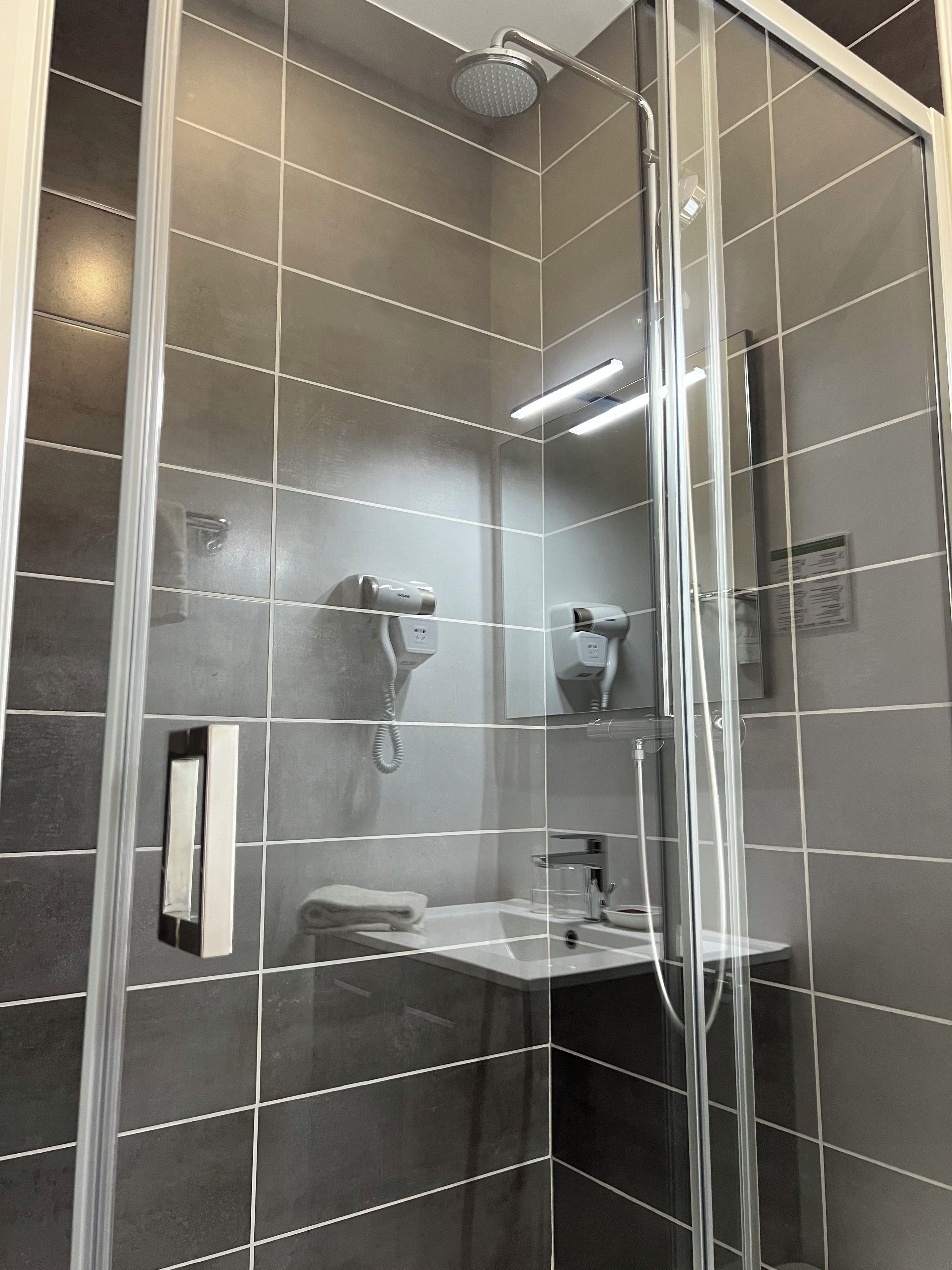 A modern shower with a glass enclosure, a handheld showerhead, and a wall-mounted hairdryer.