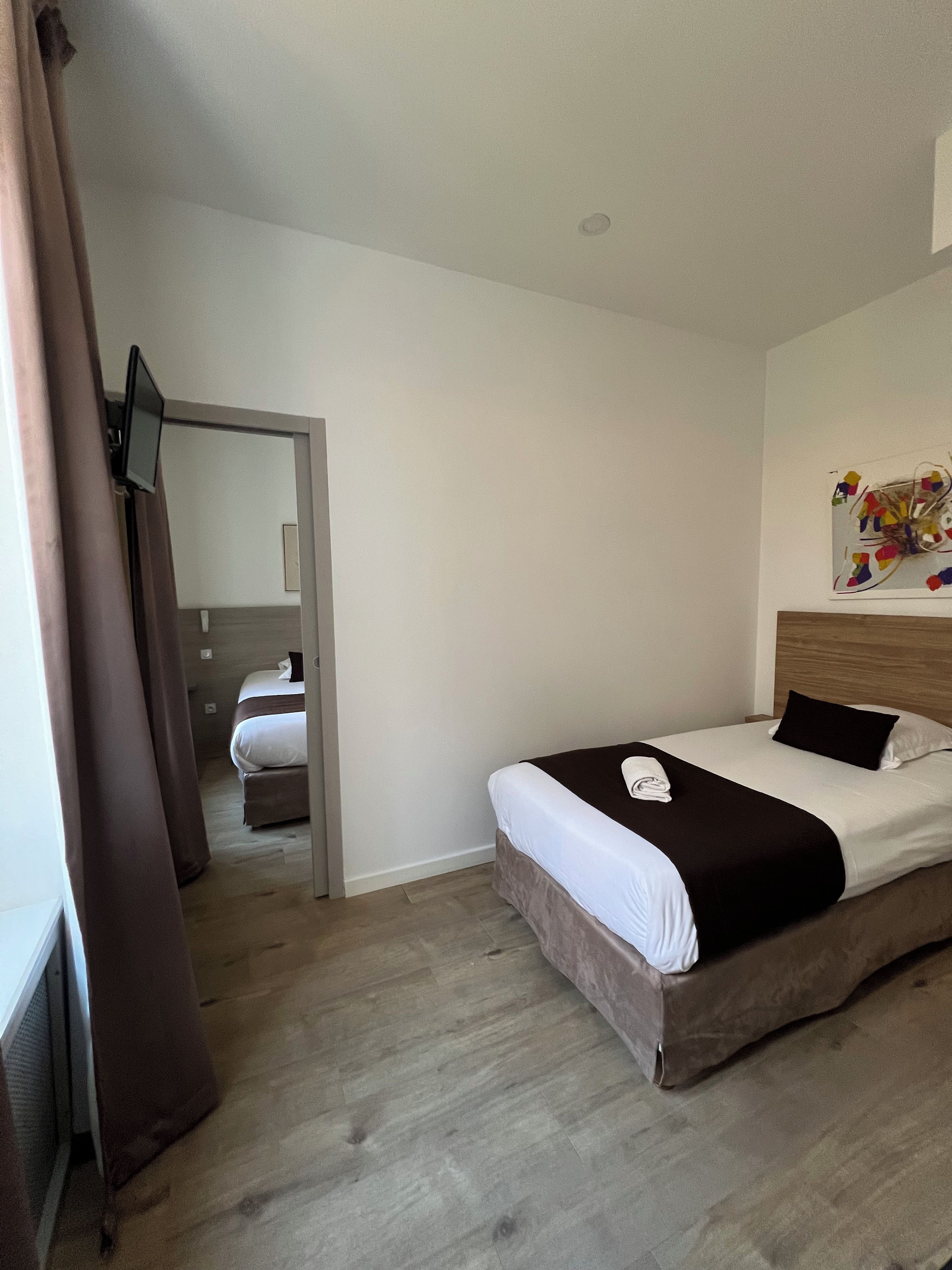 A hotel room with a bed, a flat-screen TV, a wooden headboard, and a painting on the wall.