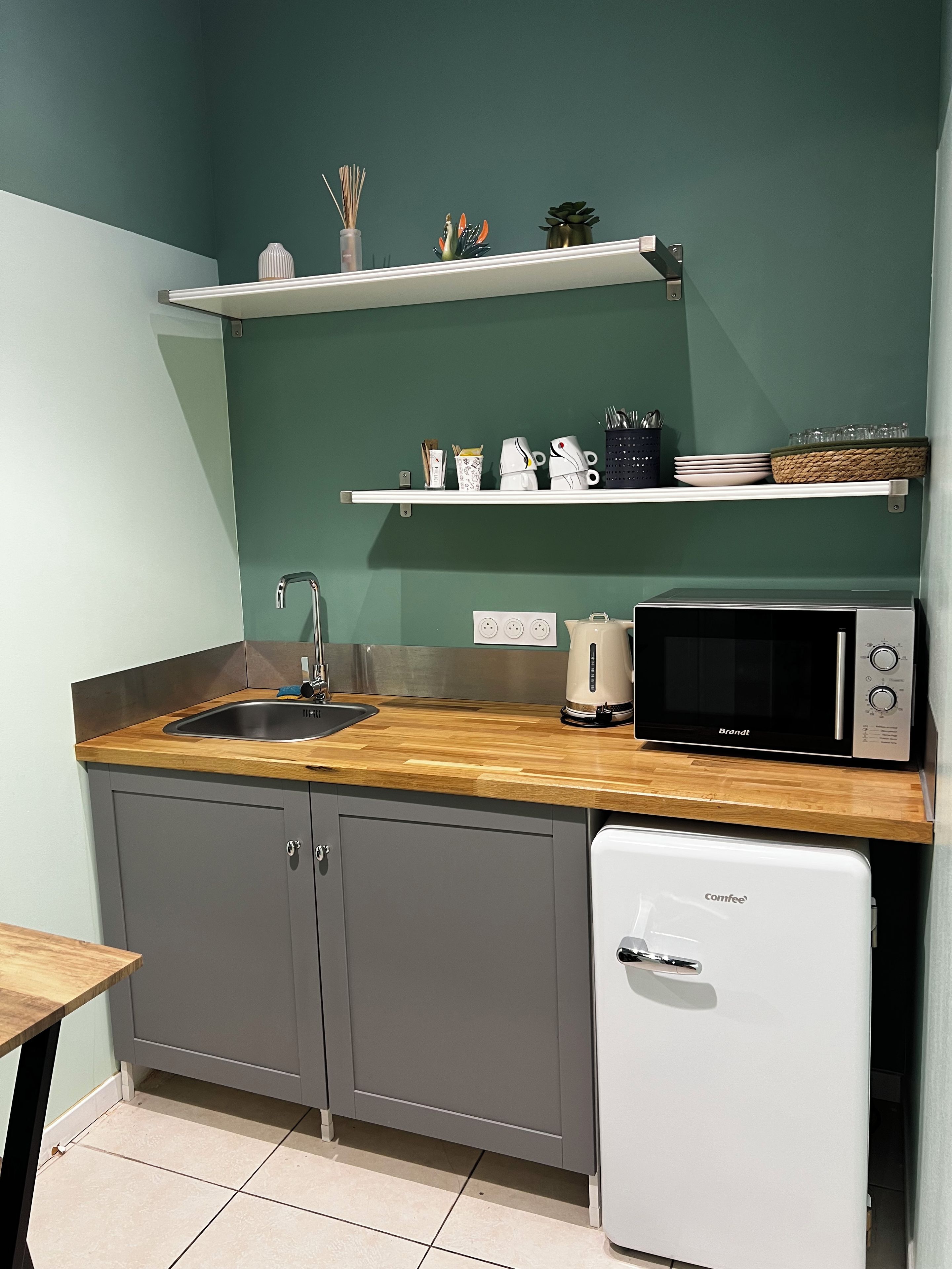 Eine kleine Küche mit Spüle, Mikrowelle, Kaffeemaschine und Kühlschrank.