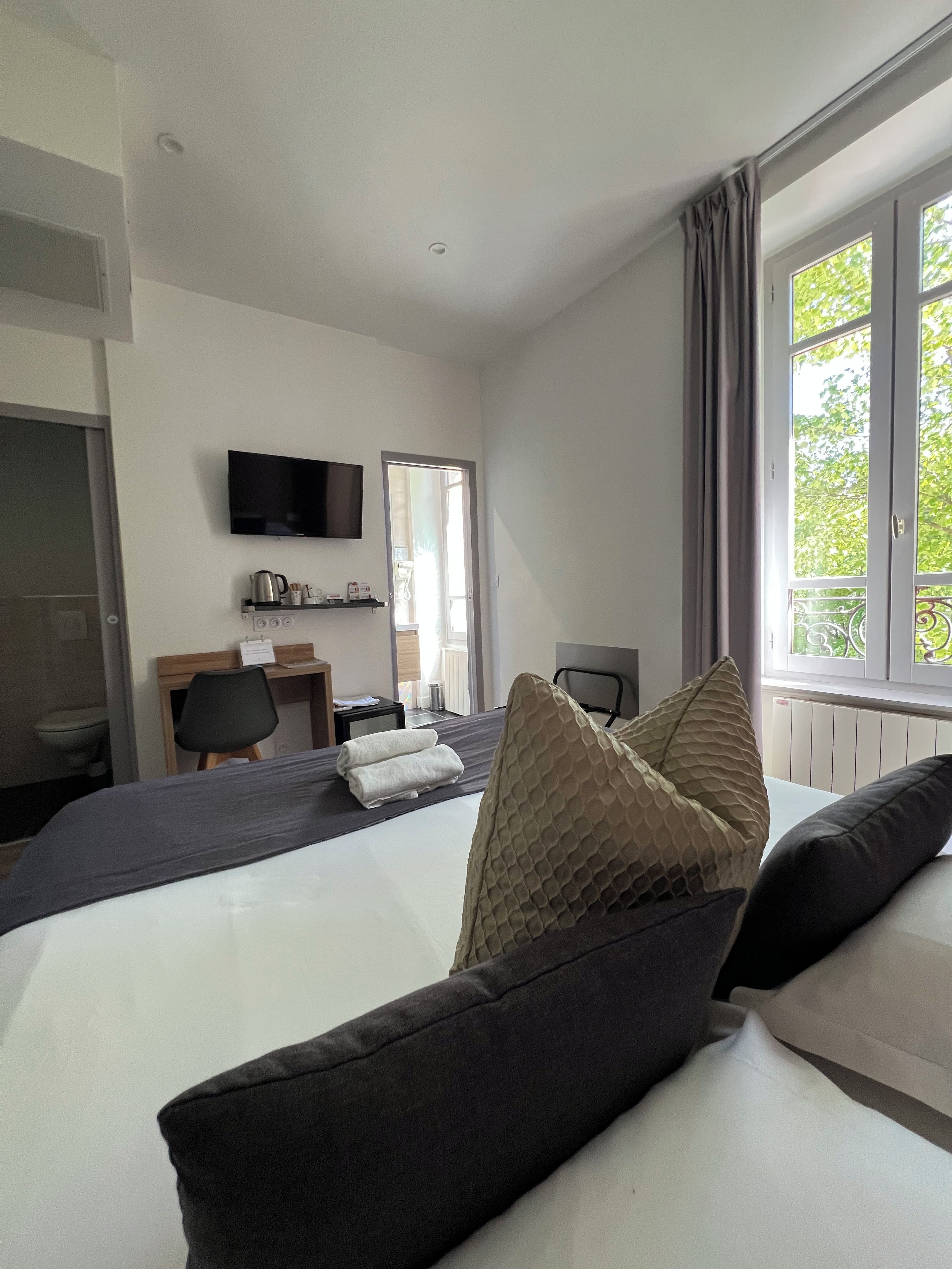 Een hotelkamer met een bed, bureau, stoel, televisie en een raam met gordijnen.