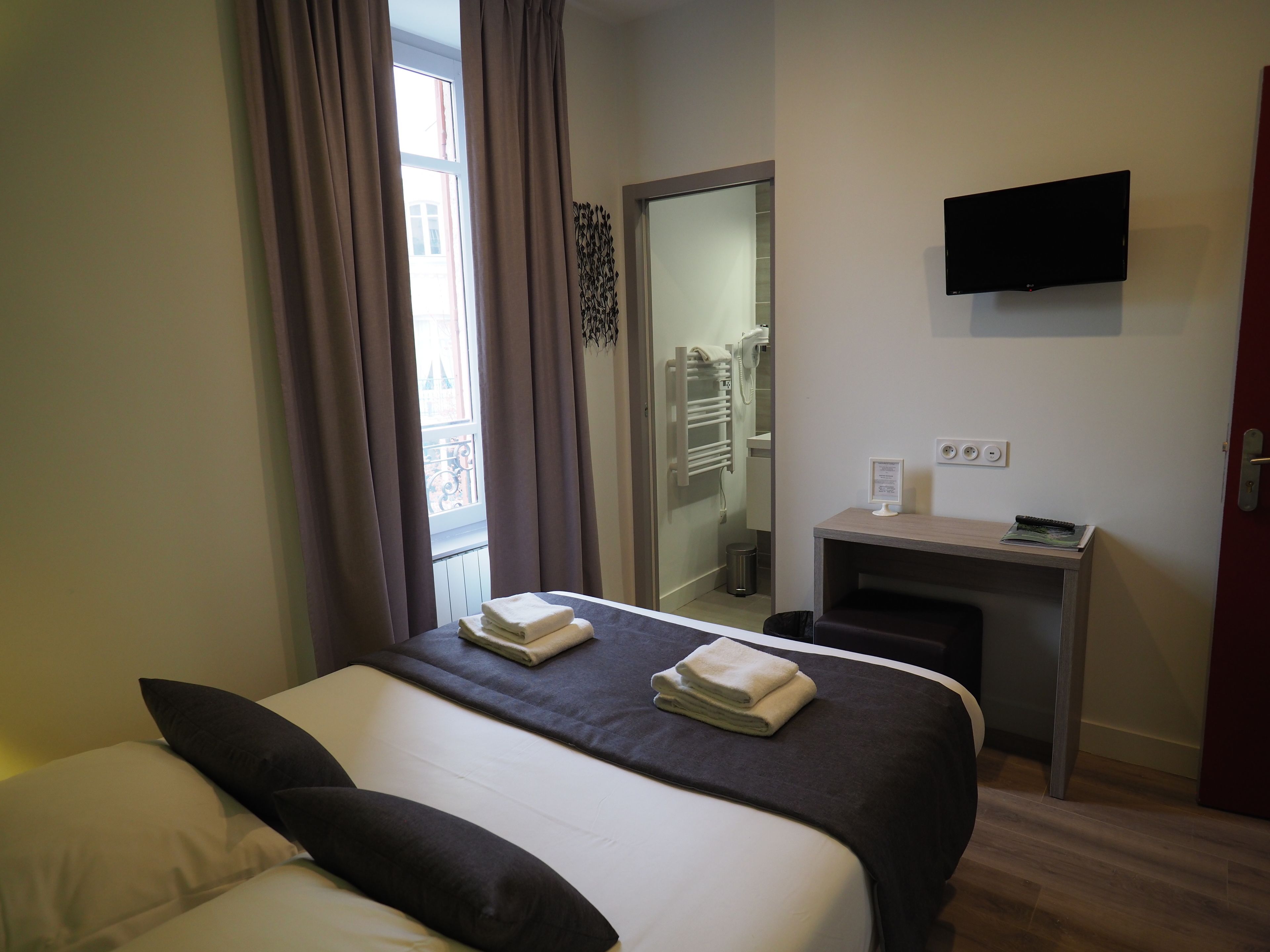 A hotel room with a bed, a desk, a TV, and a bathroom visible through a door.