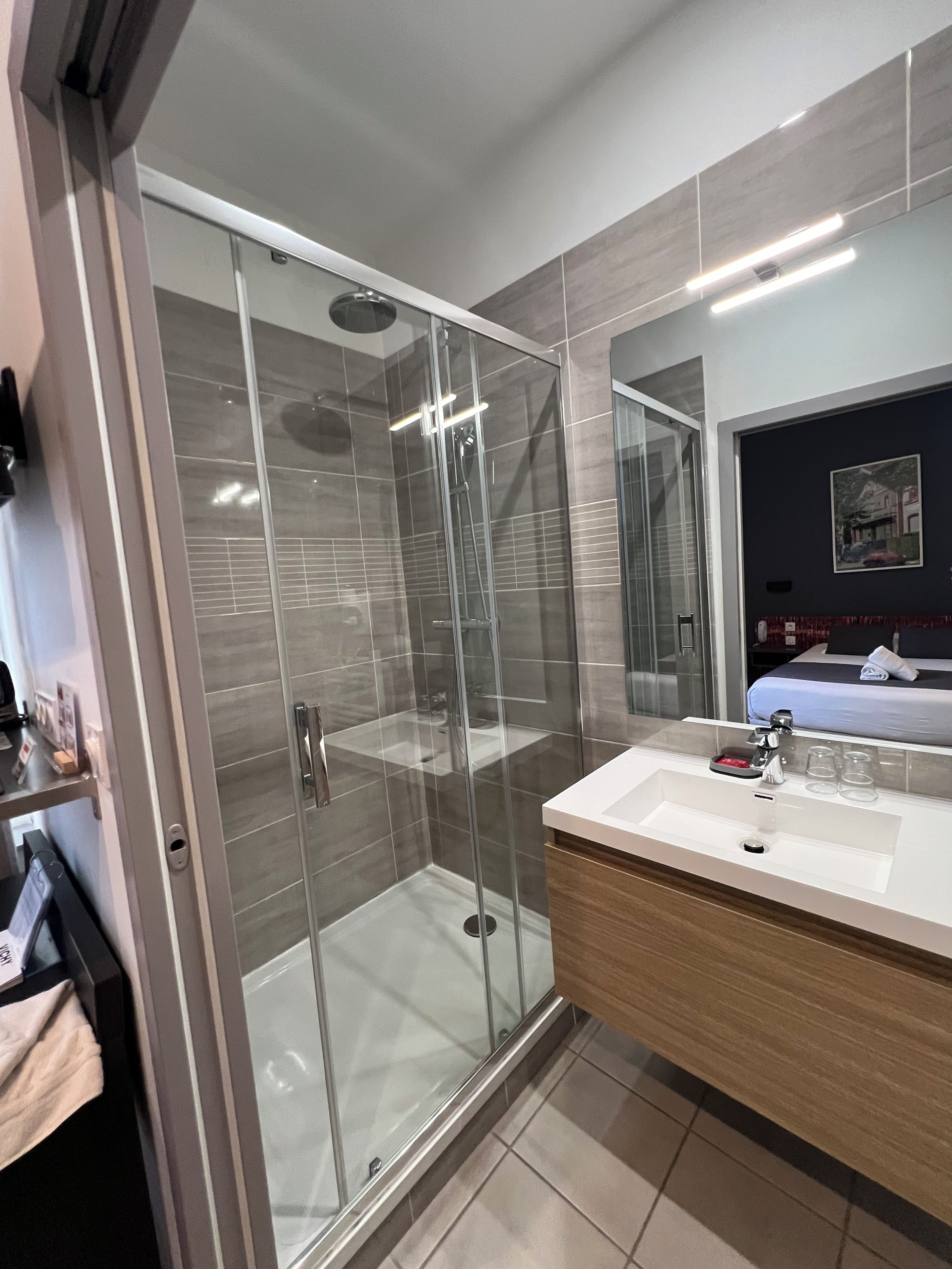 A modern bathroom with a glass-enclosed shower, a wooden vanity, and a large mirror.