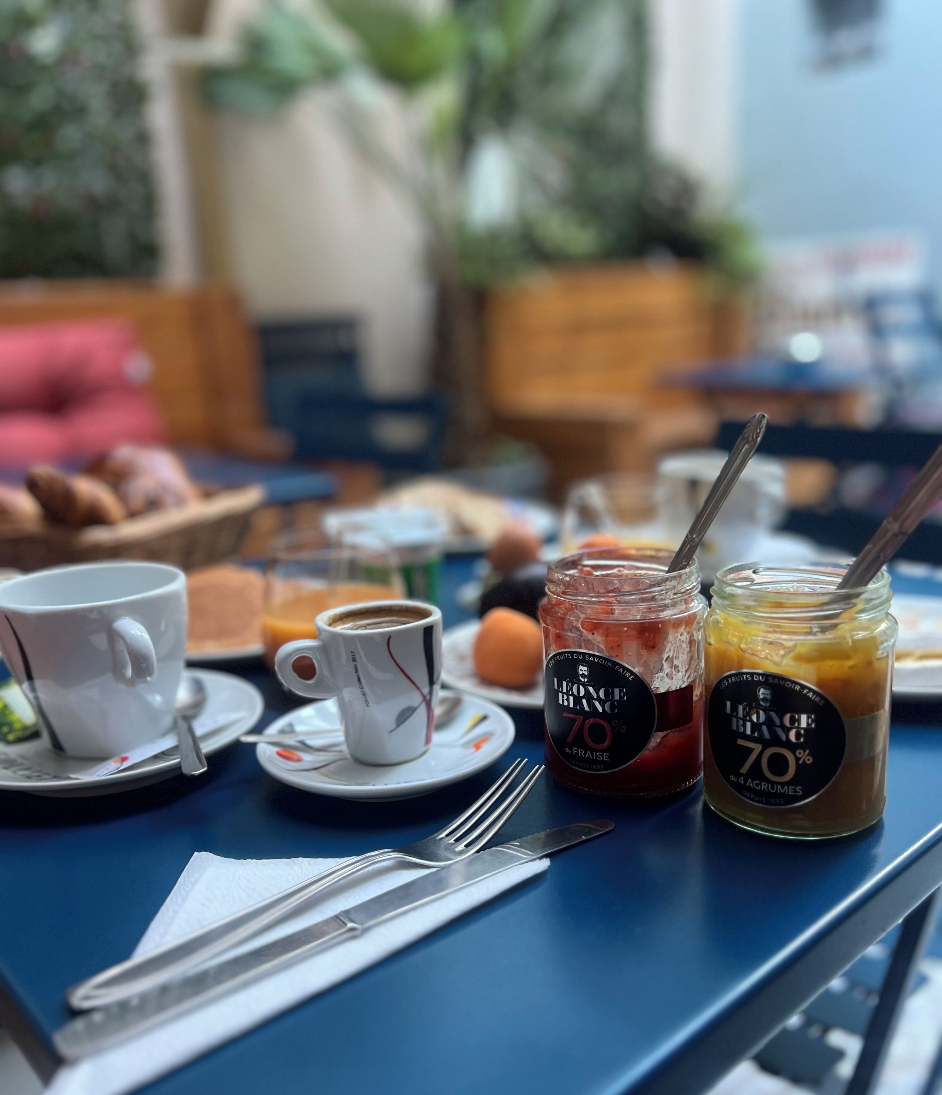 Une table dressée avec une tasse, un verre de jus, un pot de confiture et une assiette de nourriture.