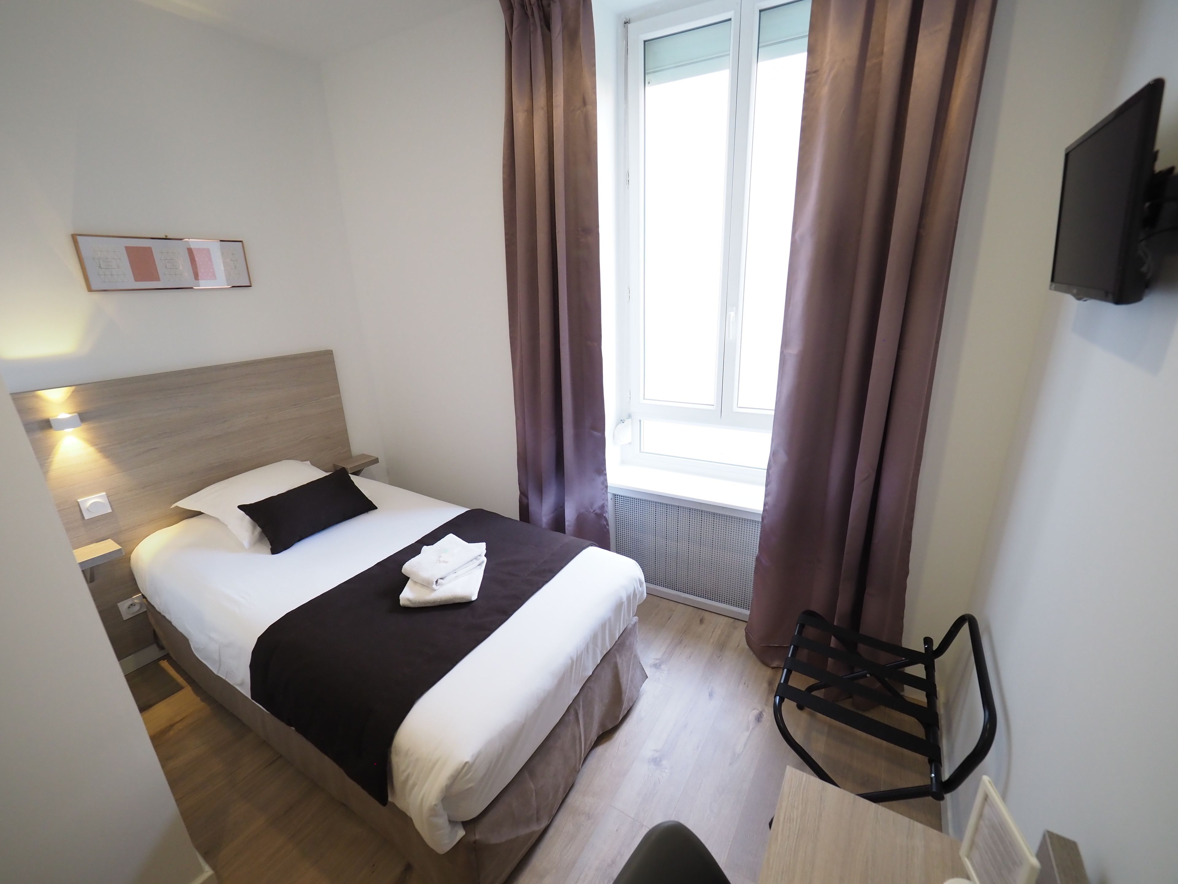 A neatly arranged hotel room with a bed, bedside table, and a chair.