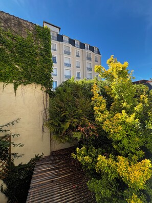A building with a white facade, a balcony, and a garden area with various plants. - Hotel Le Biarritz - Vichy (Vichy)