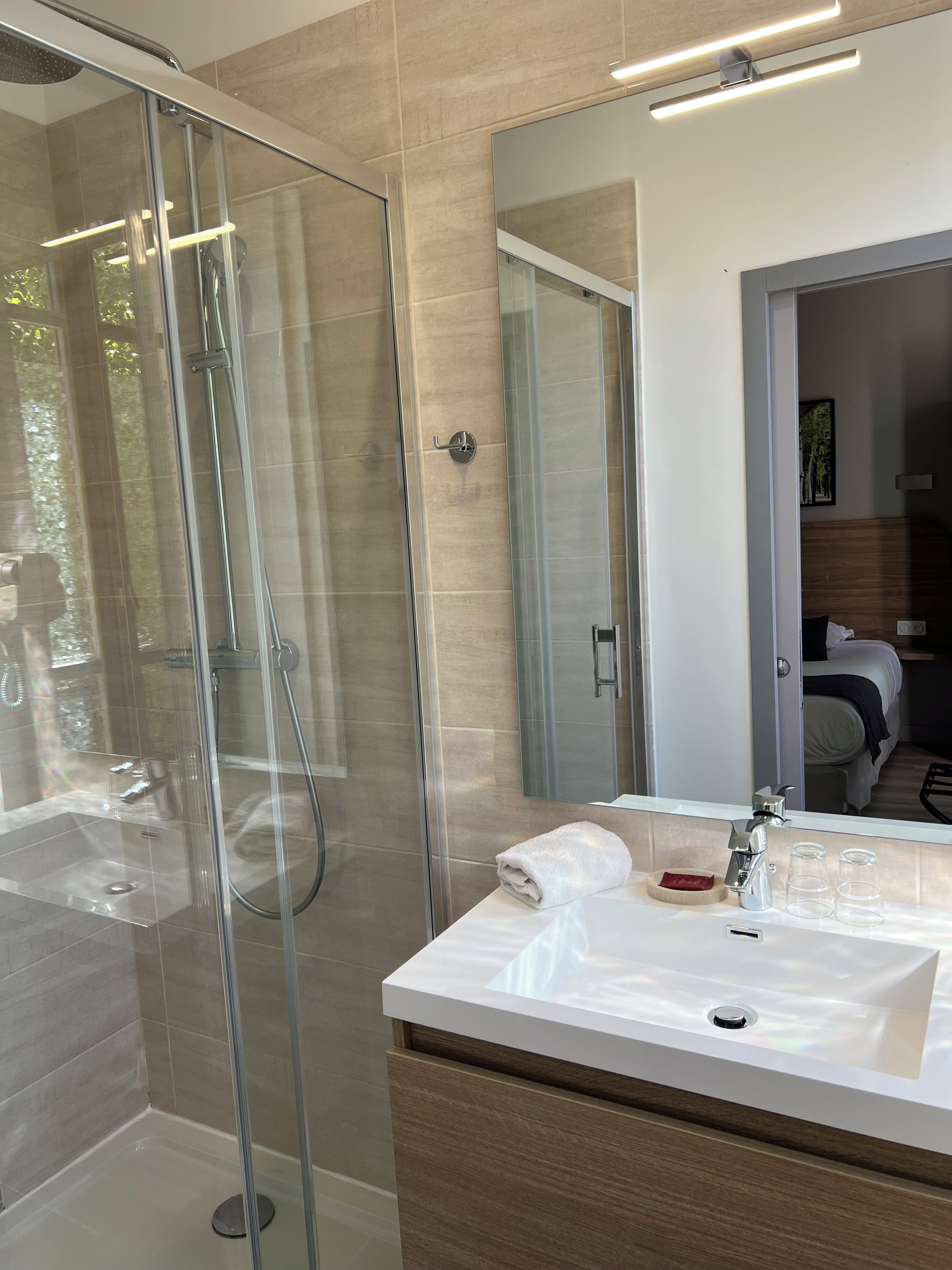Een moderne badkamer met een douchecabine van glas, een wit wastafeltje en een grote spiegel.