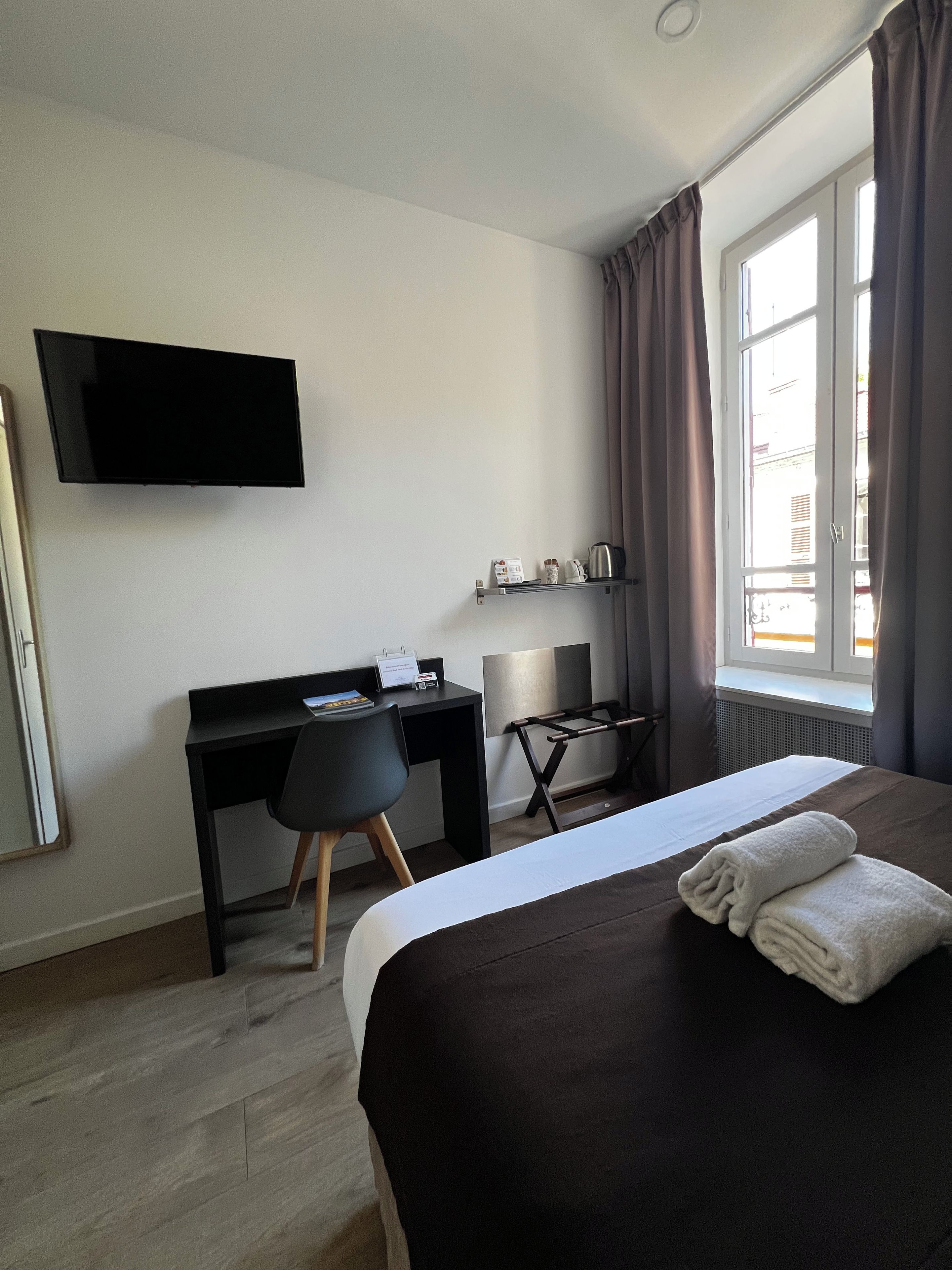A hotel room with a bed, a desk, a chair, a television, and a window with curtains.