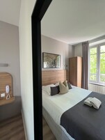Habitación de hotel con cama, cabecero de madera, armario, teléfono y ventana con cortinas.