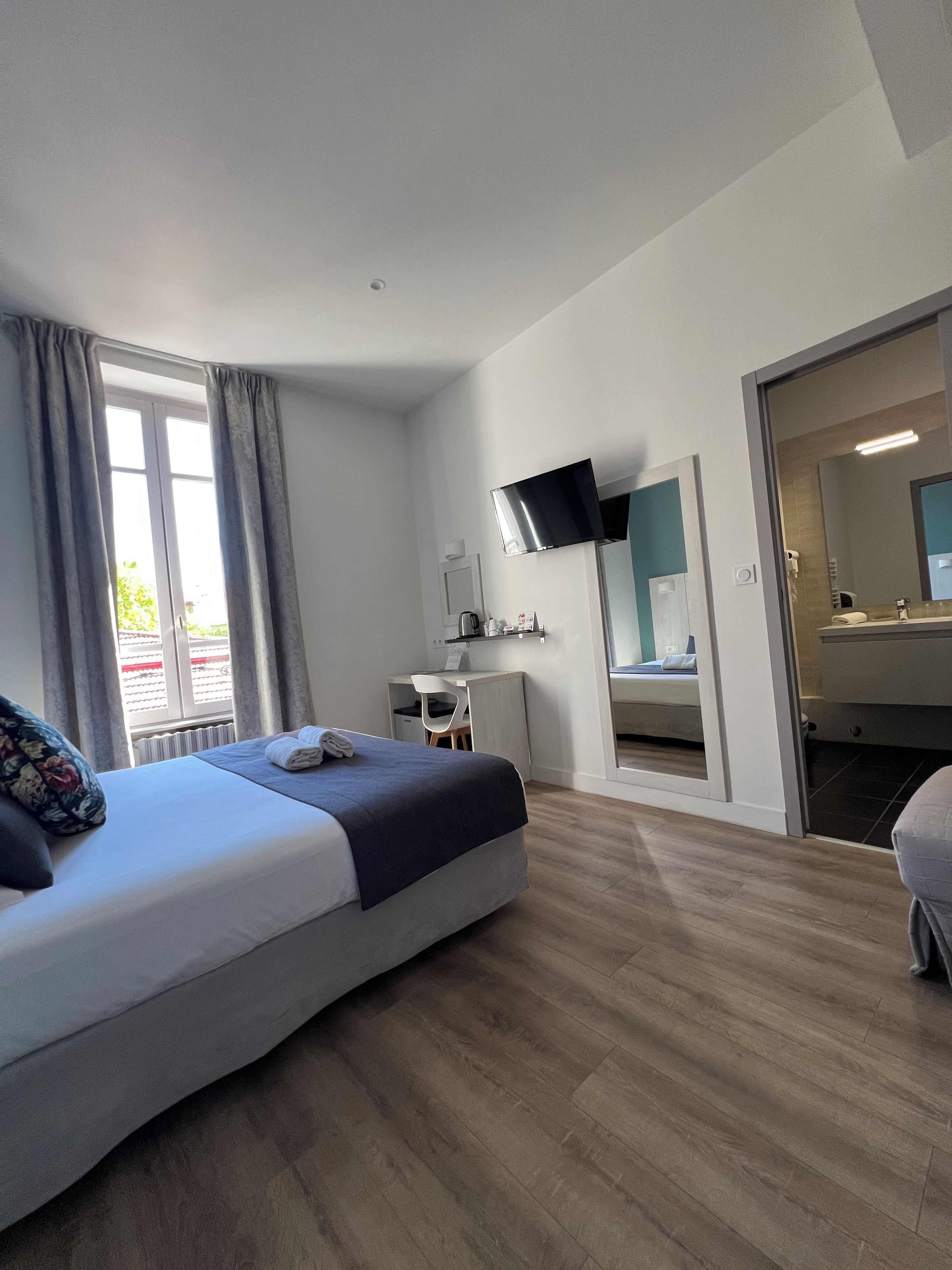 A modern hotel room with a bed, a desk, a flat-screen TV, and a bathroom visible through an open door.