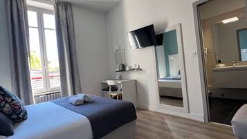 A modern hotel room with a bed, a desk, a flat-screen TV, and a bathroom visible through an open door.