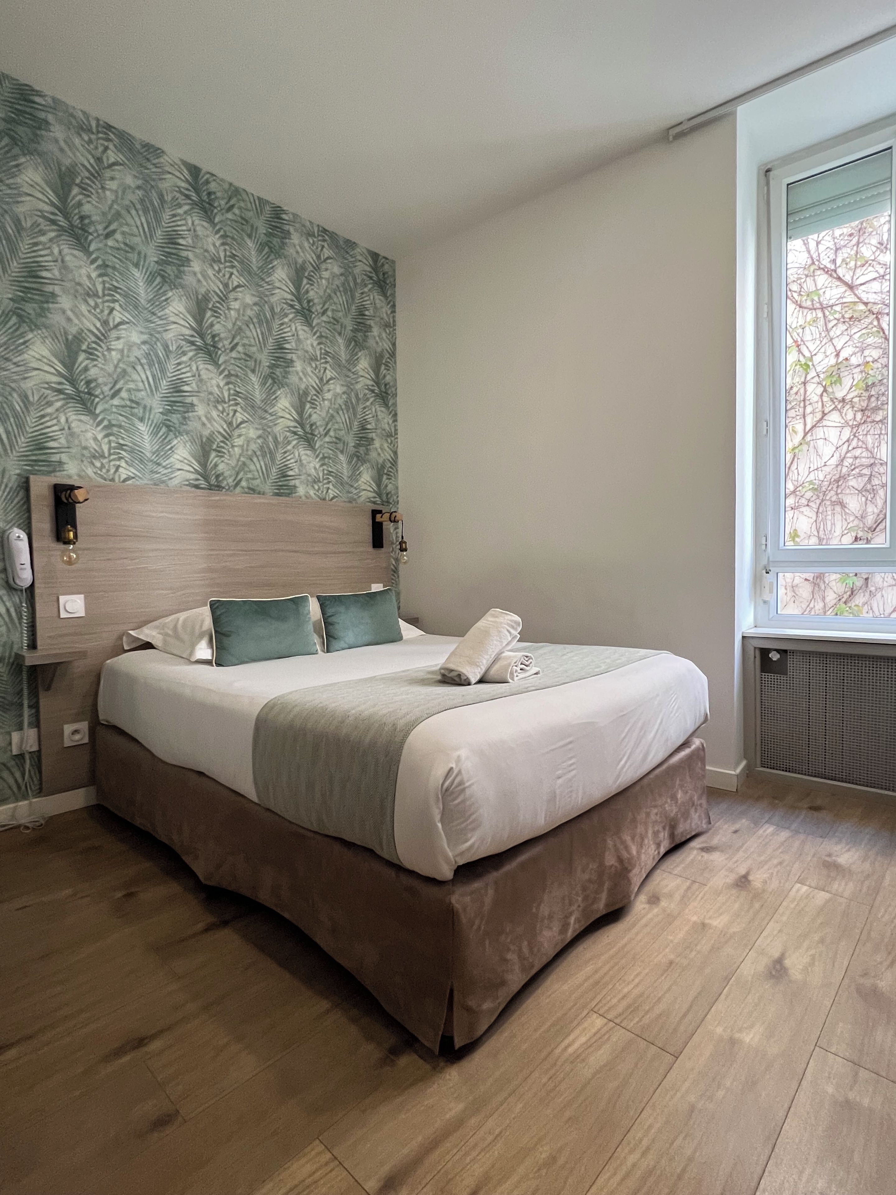 Een slaapkamer met een bed, hoofdbord, raam en een muur met bladmotief.