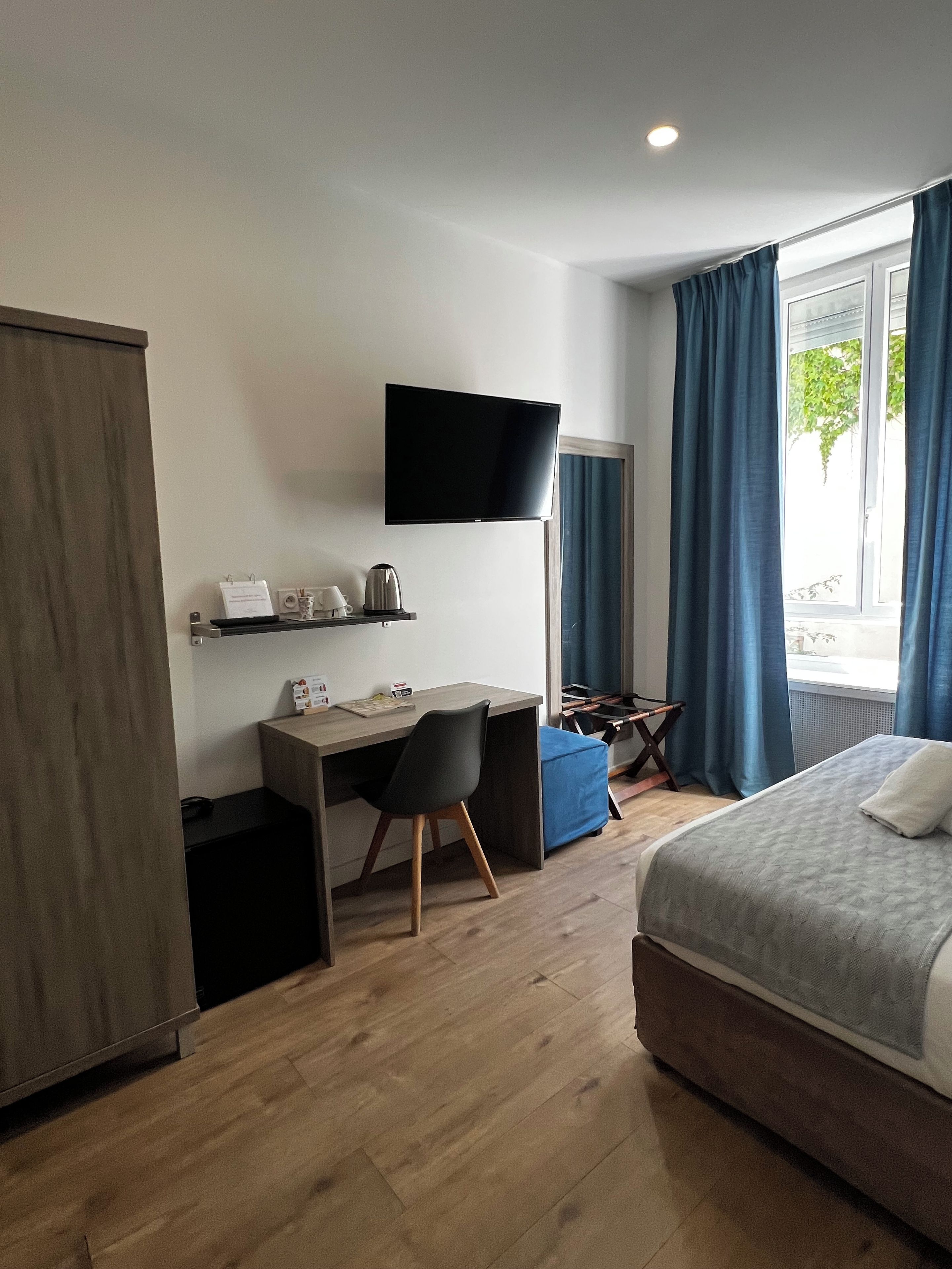 A hotel room with a bed, a desk, a chair, a television, and a window with curtains.
