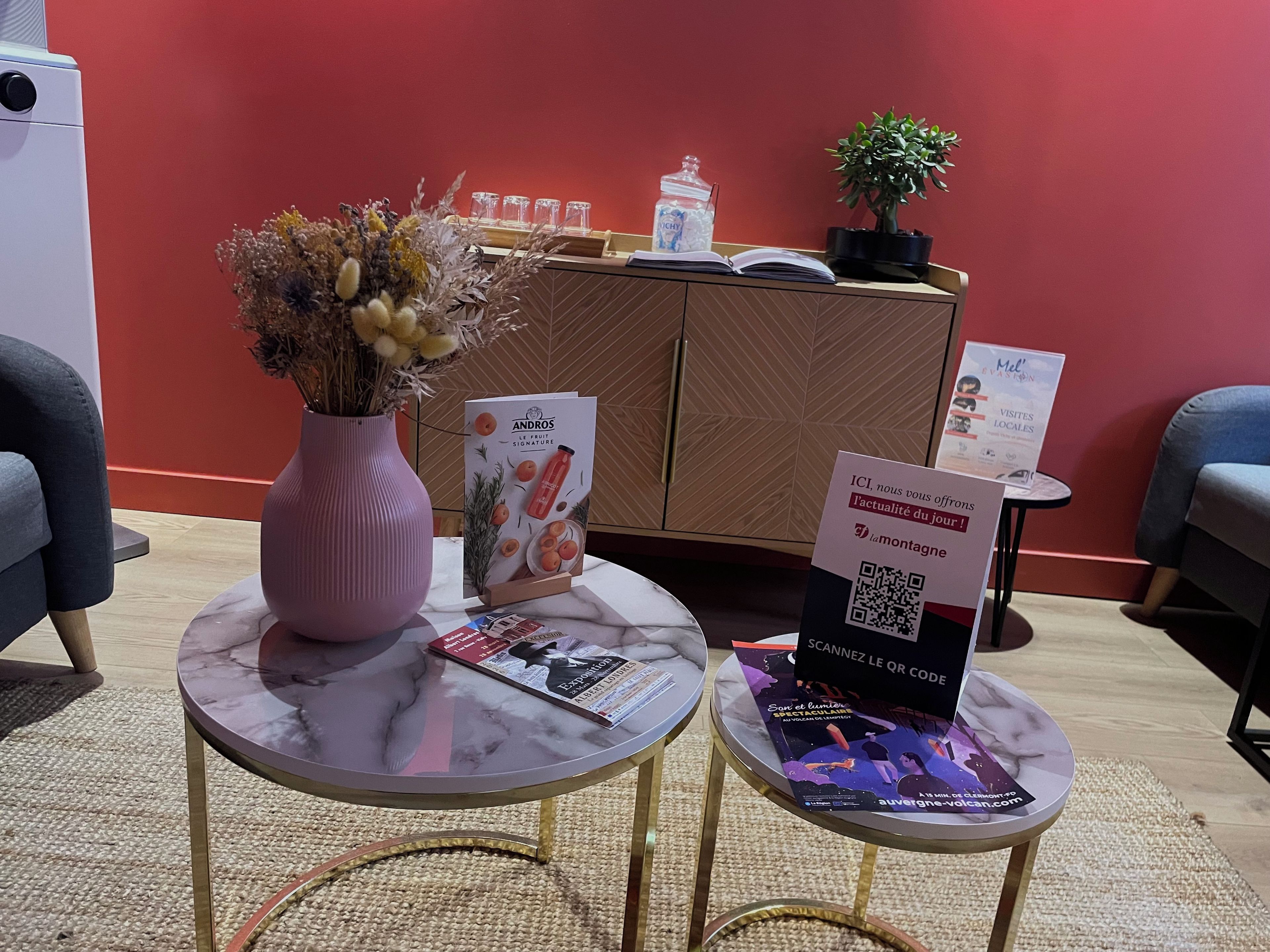 A reception area with a vase of dried flowers, a magazine, and a QR code stand.