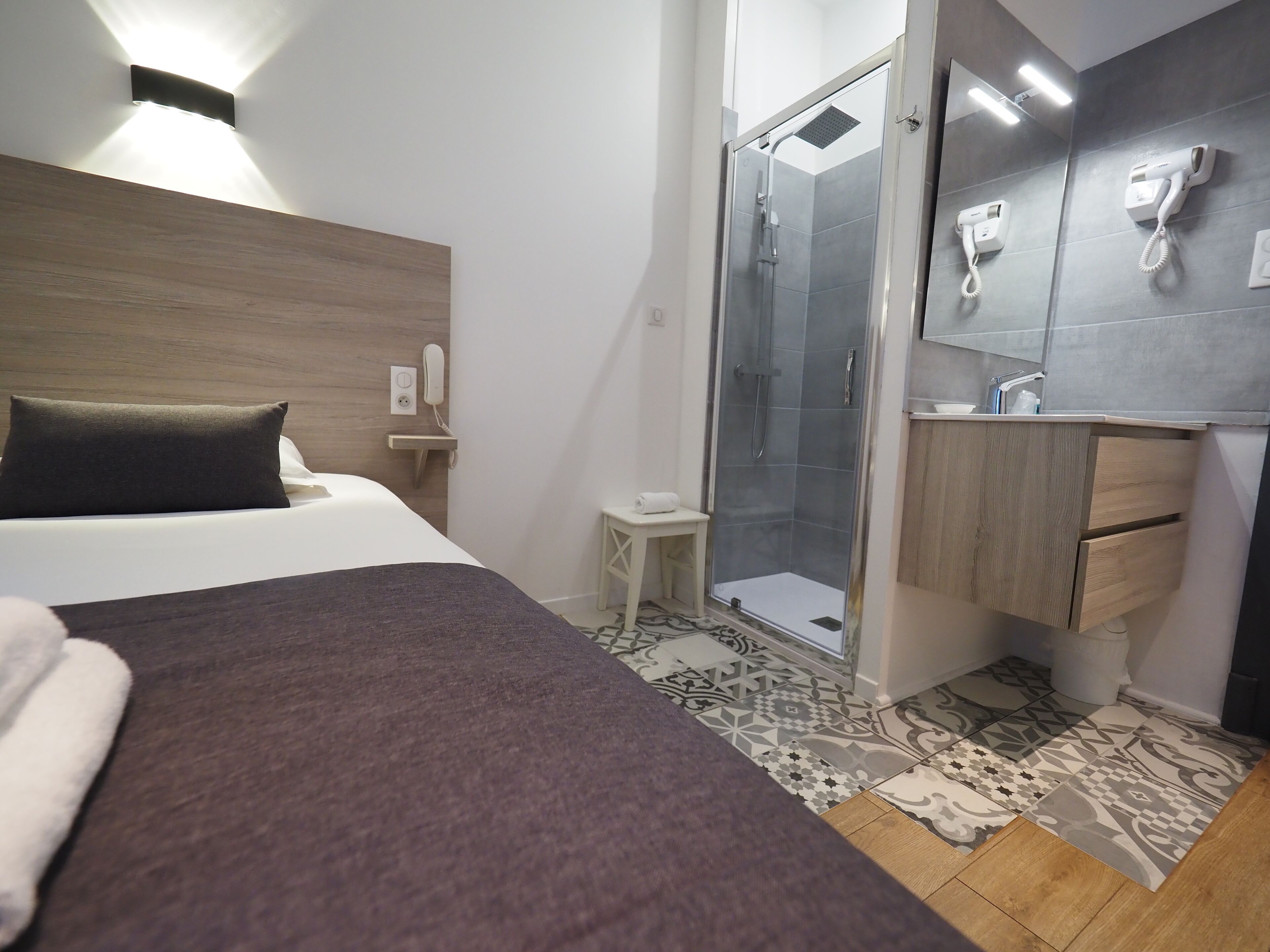 A hotel room with a bed, a shower area, a small vanity with a mirror, and a bedside table.