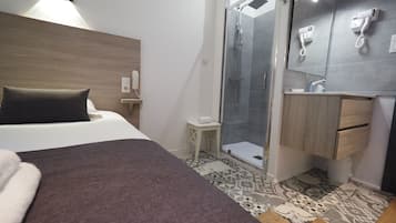 A hotel room with a bed, a shower area, a small vanity with a mirror, and a bedside table.