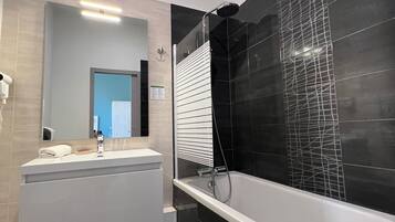 A modern bathroom with a white vanity, a large mirror, a black tiled shower enclosure, and a black tiled floor.