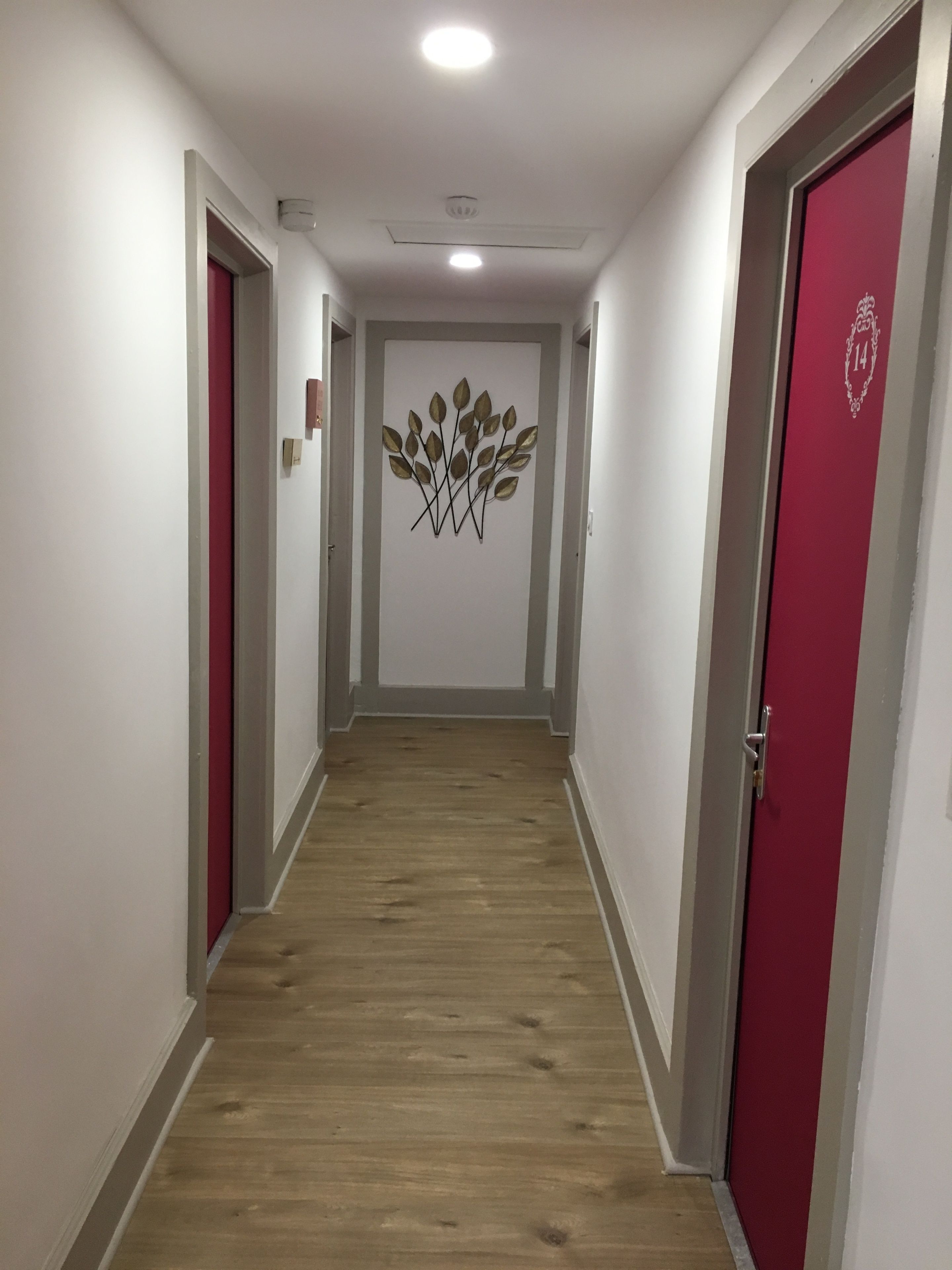 Un pasillo con suelo de madera, paredes blancas y puertas rojas.