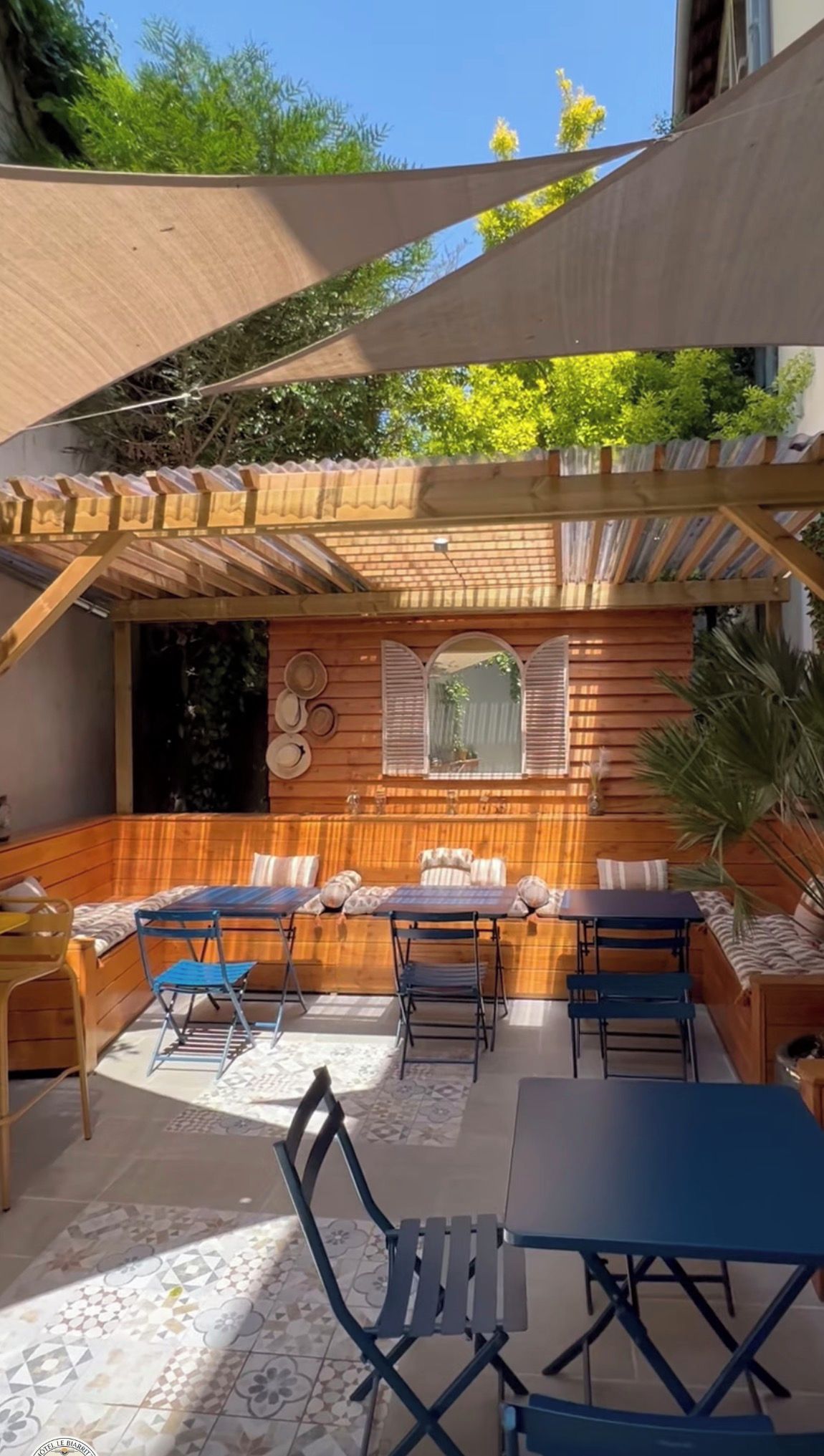 An outdoor seating area with a wooden pergola, cushioned benches, and foldable tables and chairs.