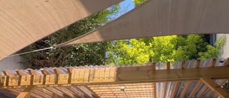 An outdoor seating area with a wooden pergola, cushioned benches, and foldable tables and chairs.