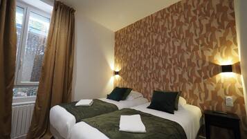 Une chambre d’hôtel avec deux lits, une fenêtre avec des rideaux, un papier peint à motifs et des lampes fixées au mur.