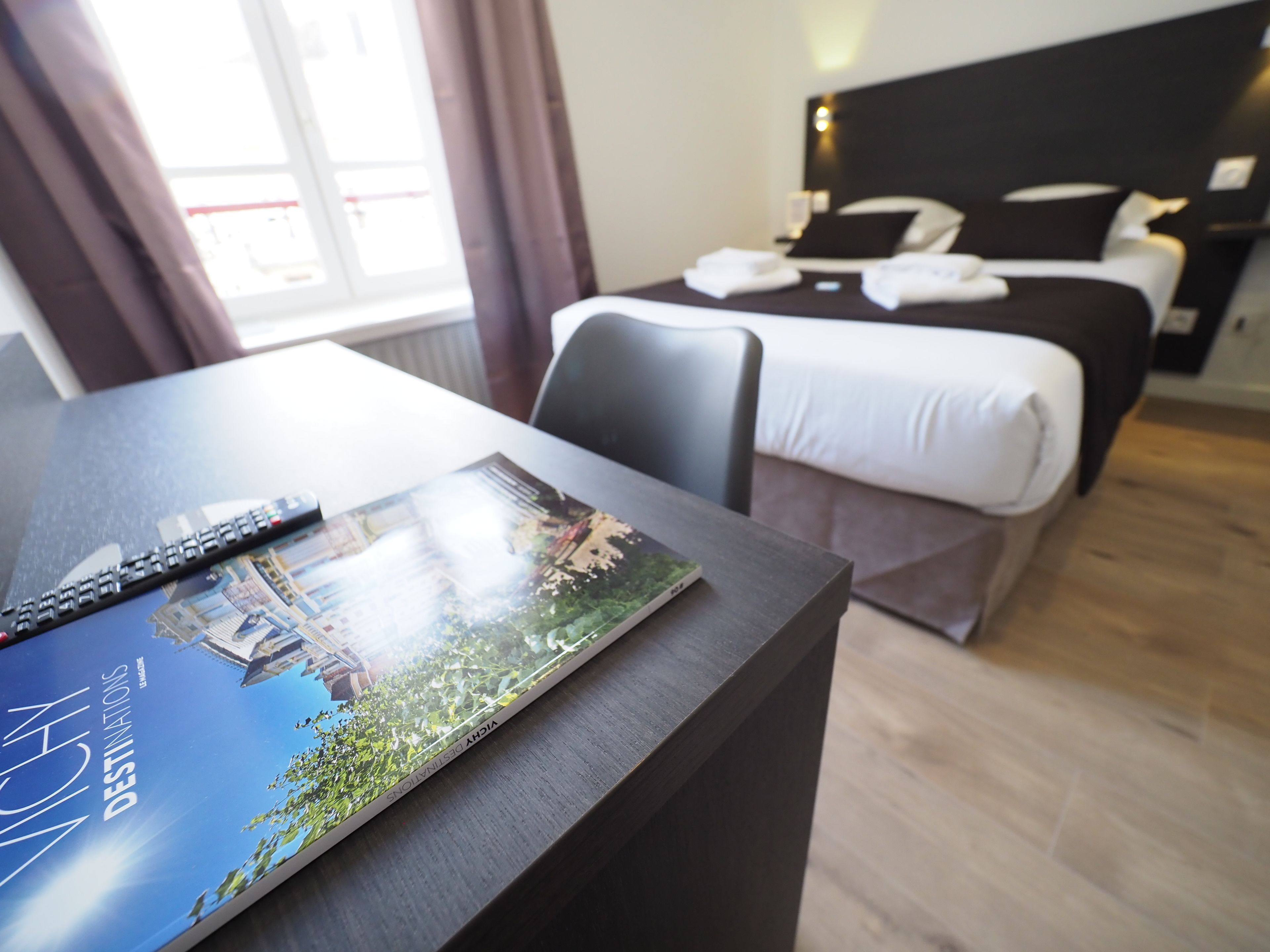 Una habitación de hotel con una cama, un escritorio con un control remoto y un libro sobre el escritorio.