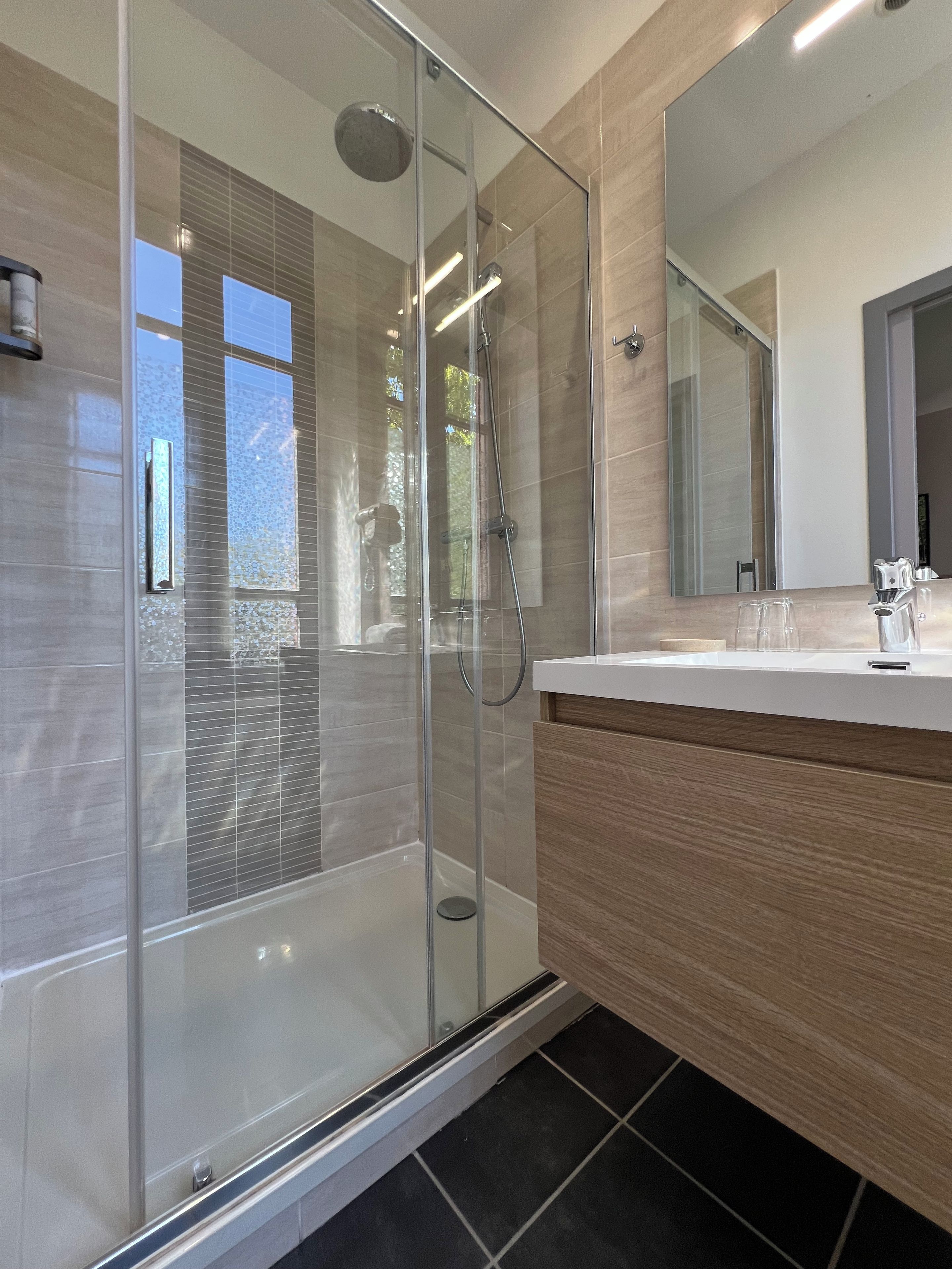 Un baño moderno con ducha de vidrio, tocador de madera y un espejo grande.