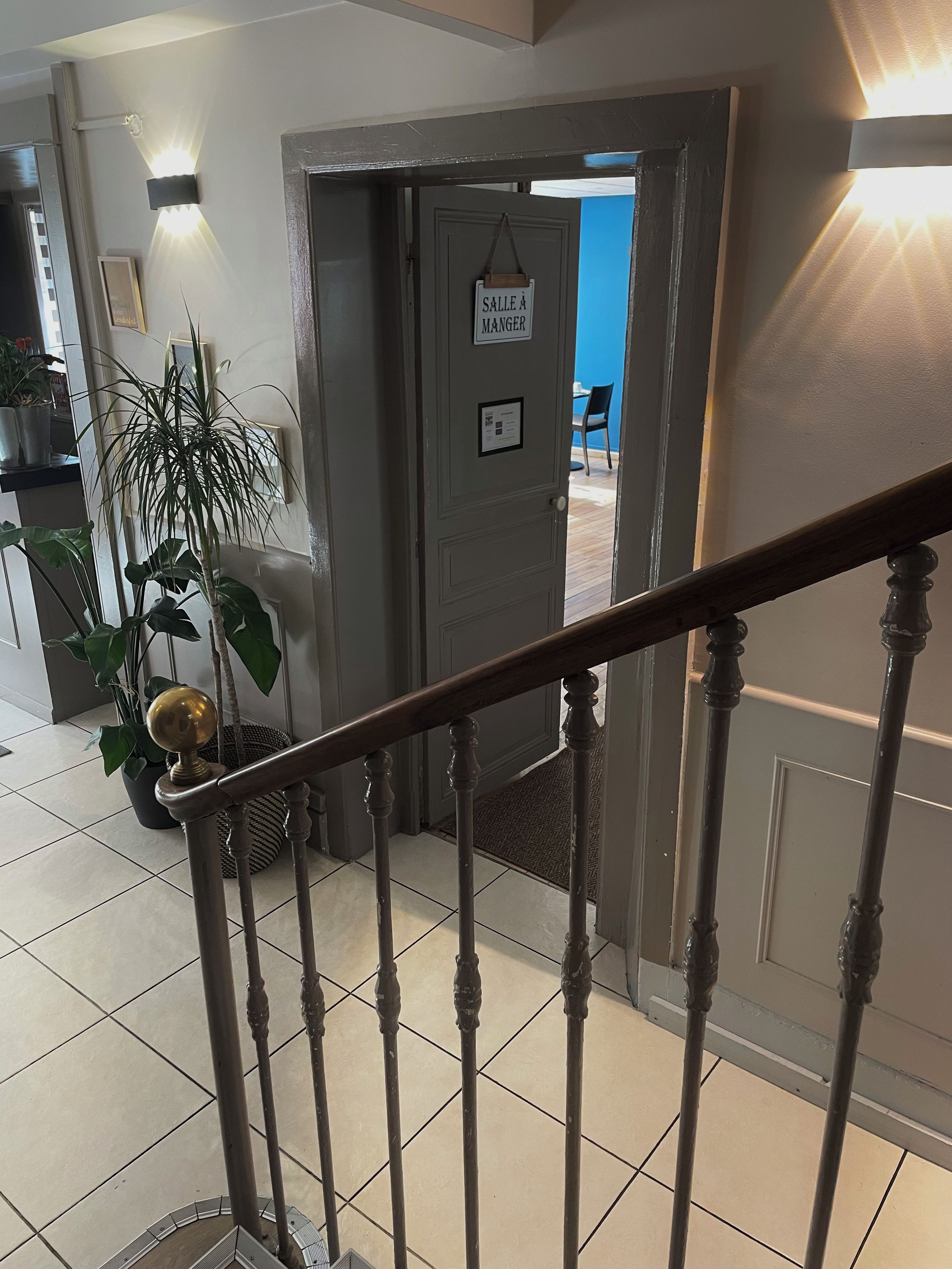 A staircase with a handrail, a door with a sign reading 'SALLE À MANGER,' and a potted plant.