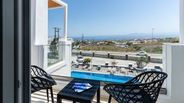A balcony with a view of a swimming pool, a street, and distant mountains. - Golden Star (Santorini)