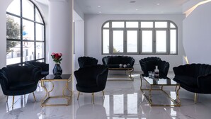 A modern interior with a large arched window, black upholstered chairs, a glass coffee table, and a vase with flowers. - Golden Star (Santorini)