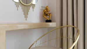 A modern room with a gold-framed chair, a decorative mirror, and a golden statue on a white console table. - Golden Star (Santorini)