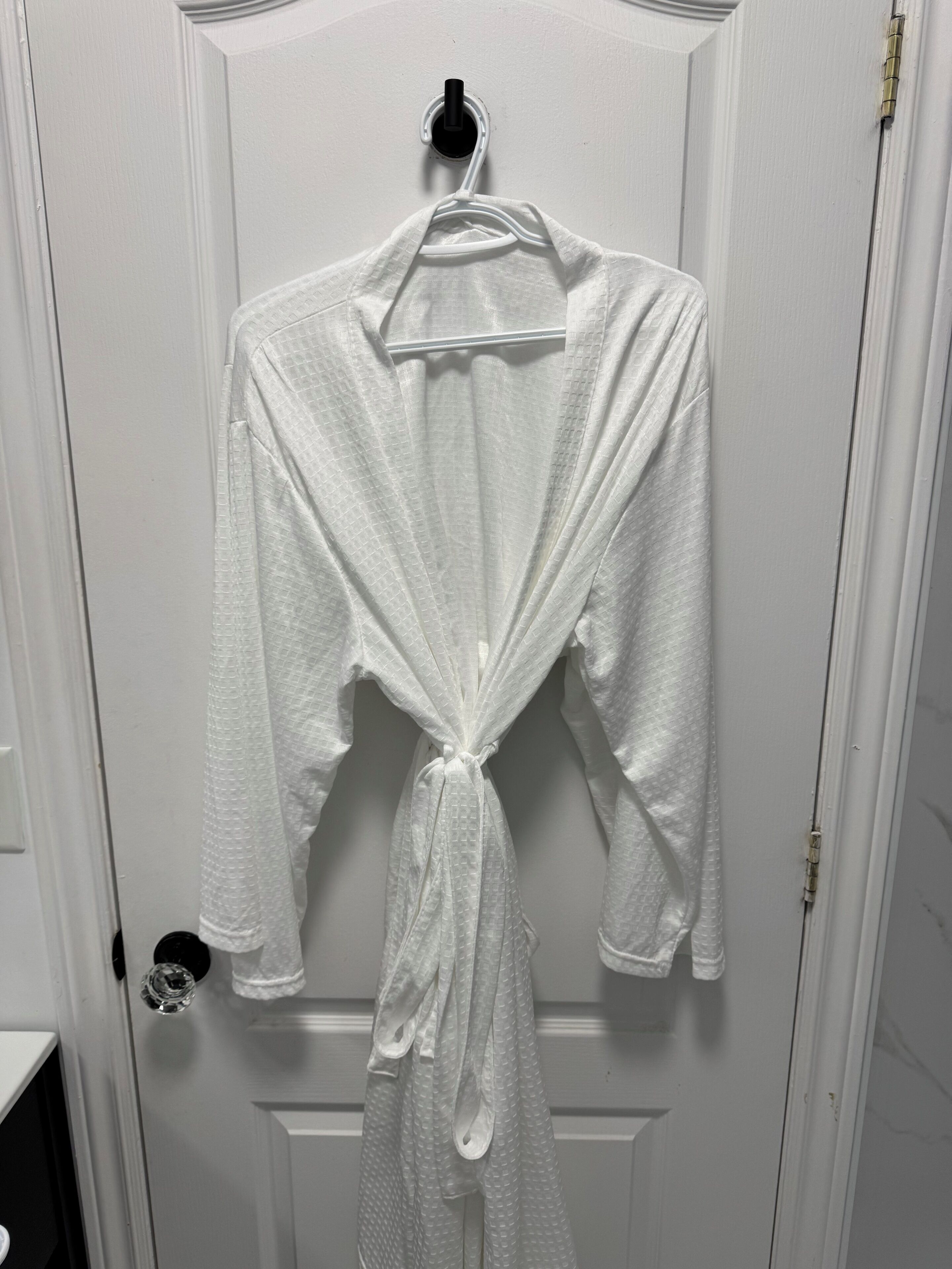 A white robe hanging on a door with a black hanger.