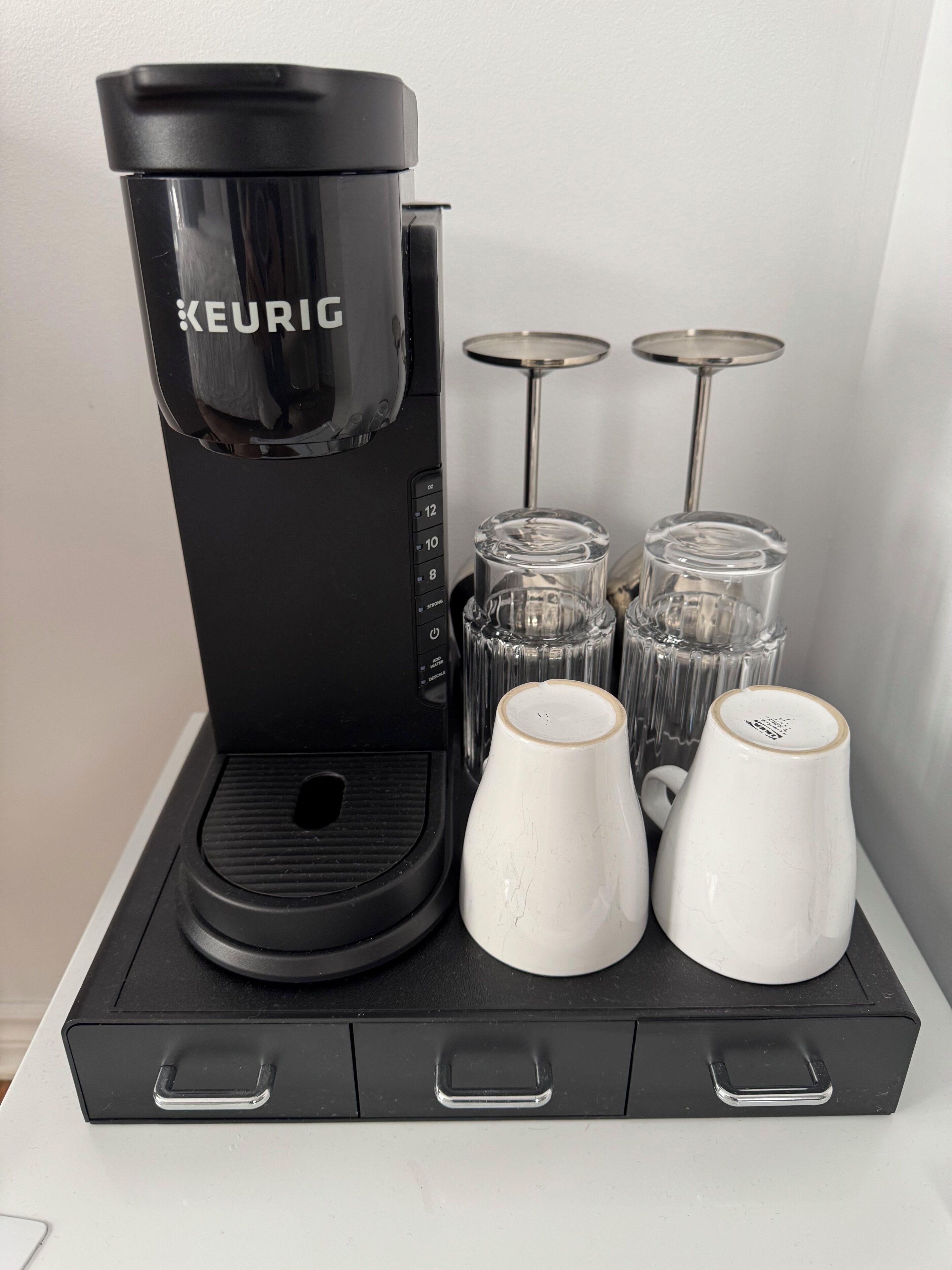 Una cafetera Keurig con cuatro jarros y dos tazas sobre una bandeja negra.