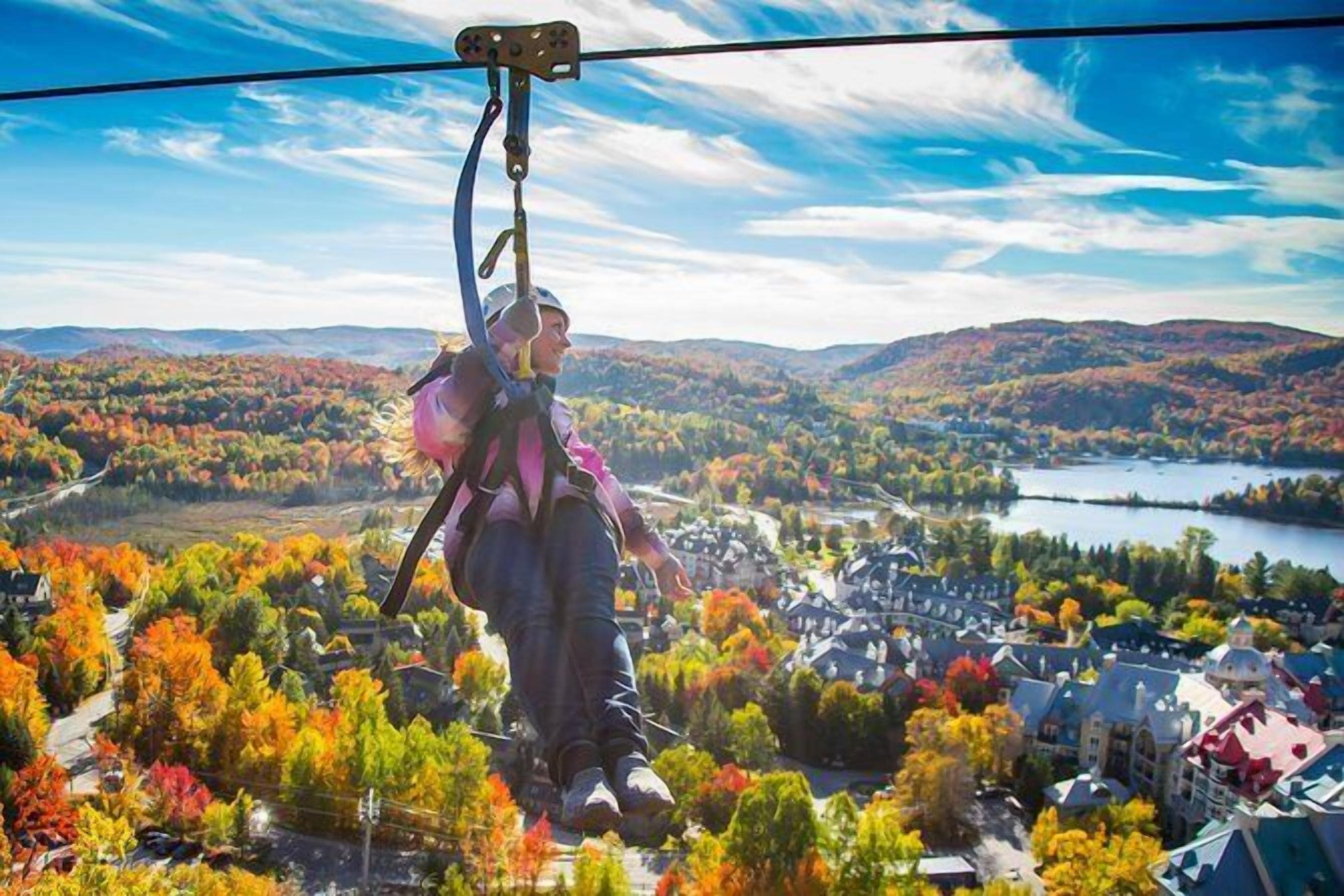 A person on a zip line with a scenic view of a town and autumn foliage.