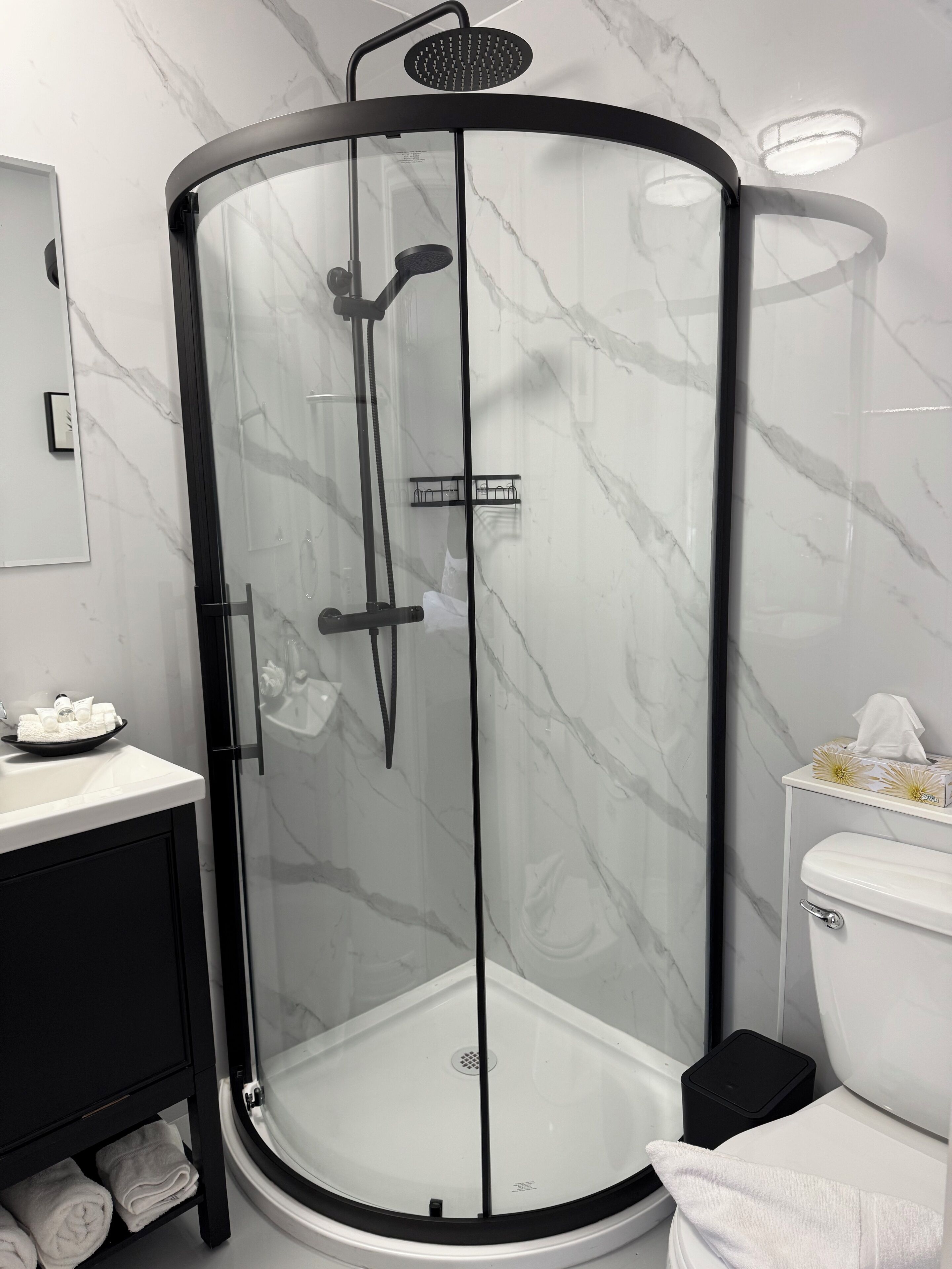 A modern bathroom with a glass-enclosed shower, a white toilet, and a black cabinet with towels.