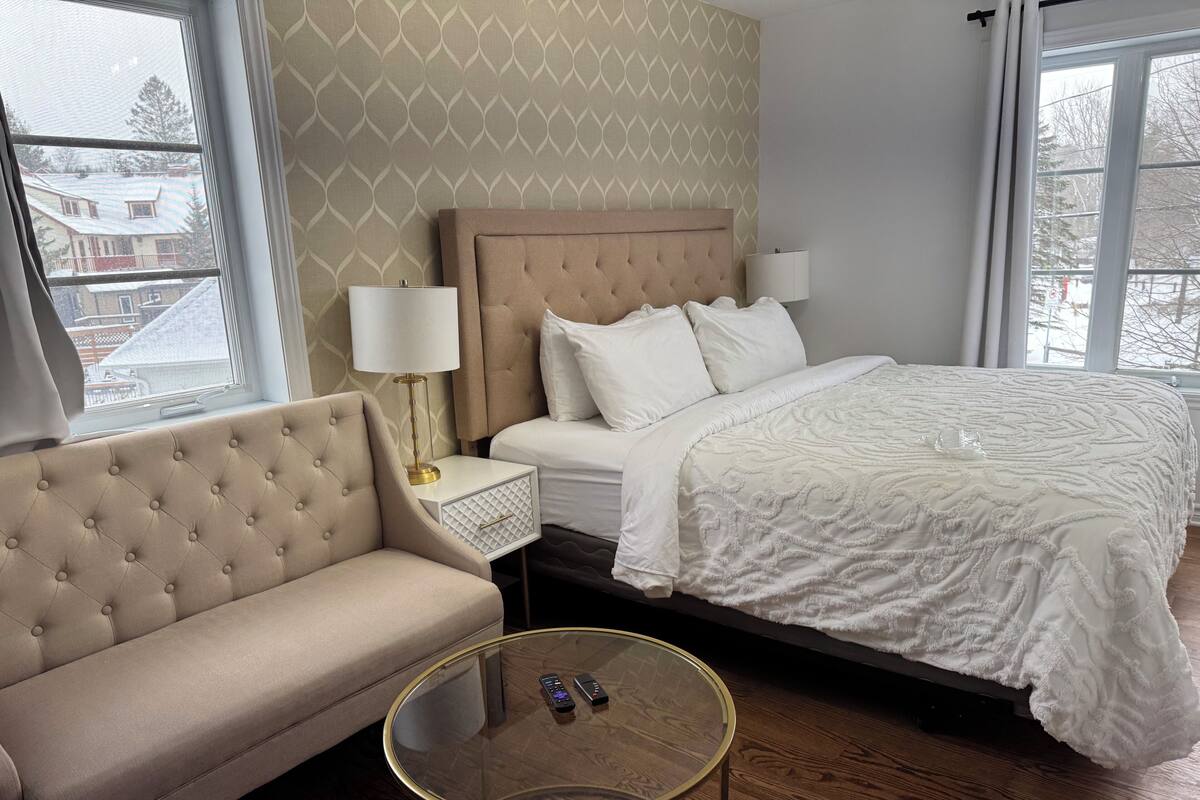 A hotel room with a bed, a sofa, a bedside table with a lamp, and a glass coffee table.
