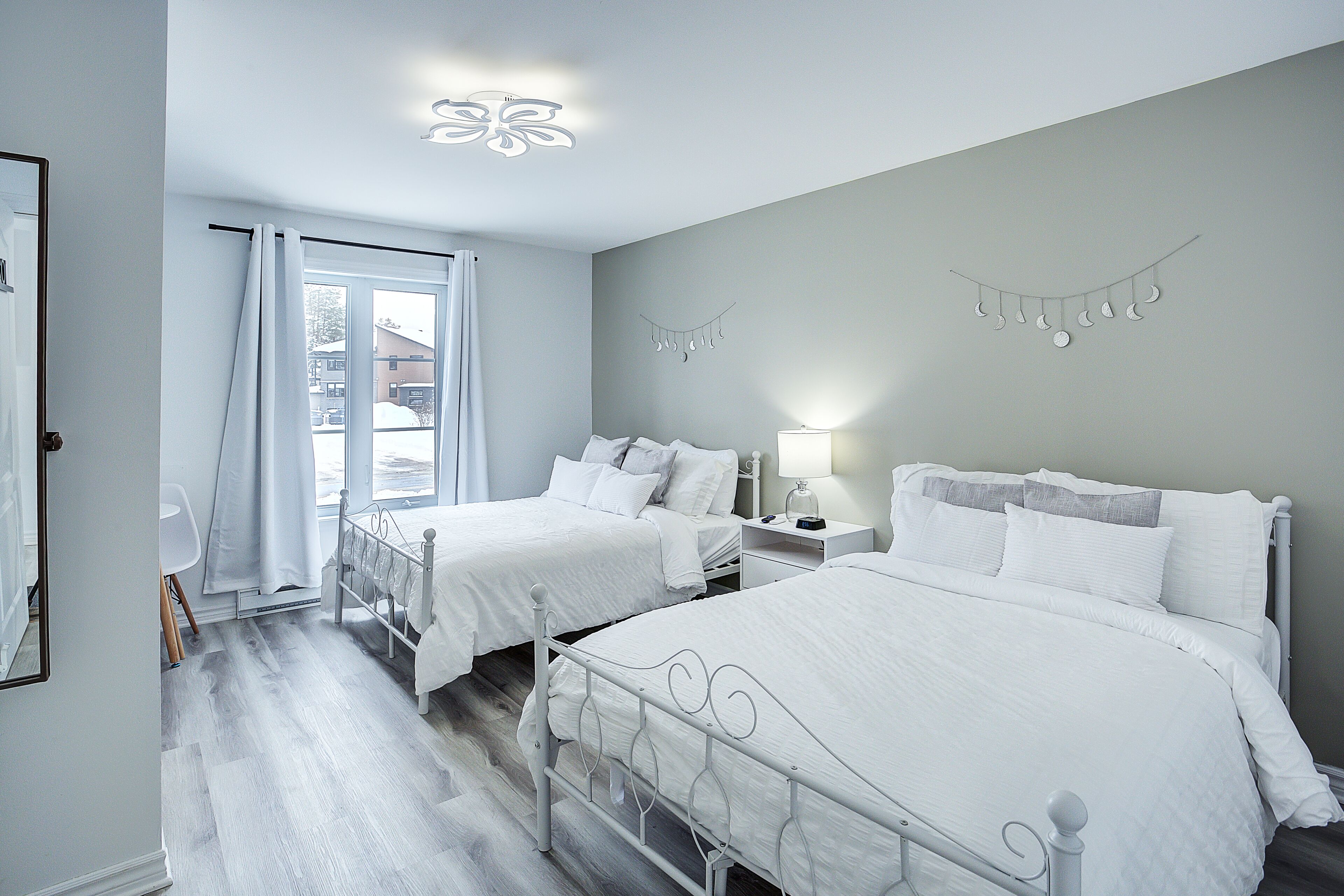 Une chambre avec deux lits, une fenêtre avec des rideaux, une table de chevet avec une lampe et un élément décoratif fixé au mur.