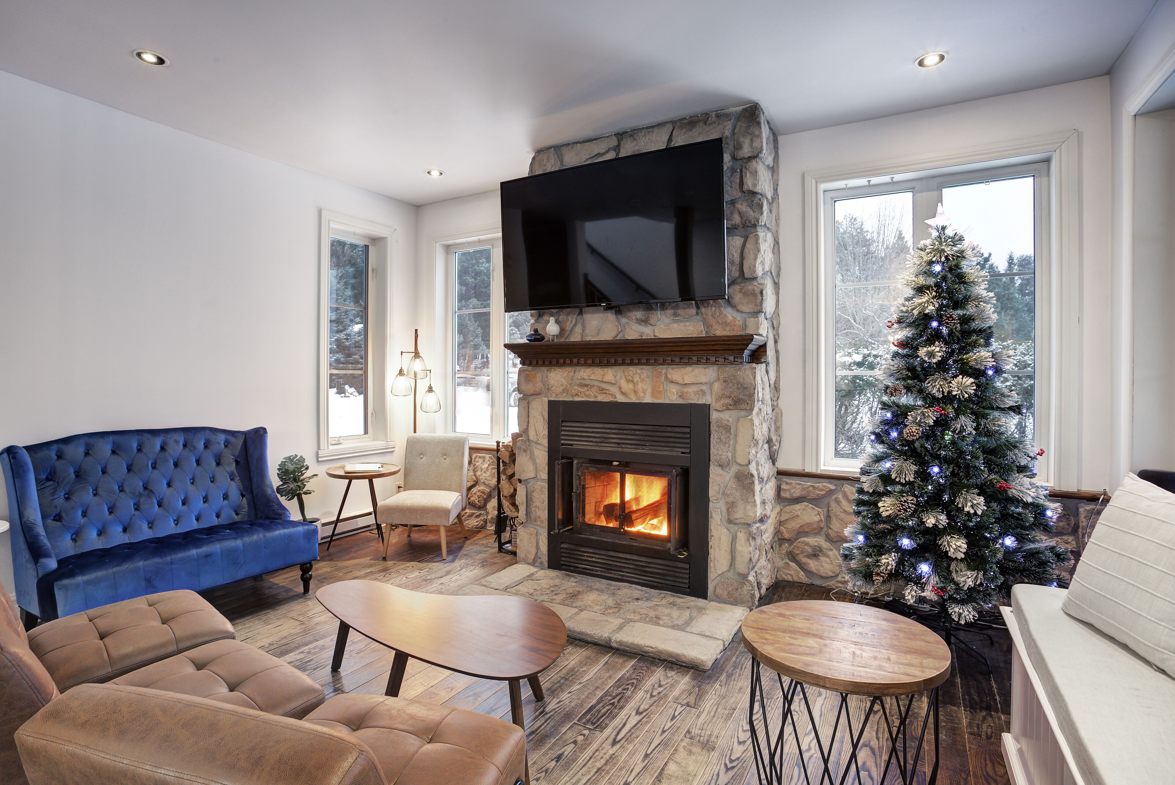 A living room with a stone fireplace, a blue sofa, and a Christmas tree.