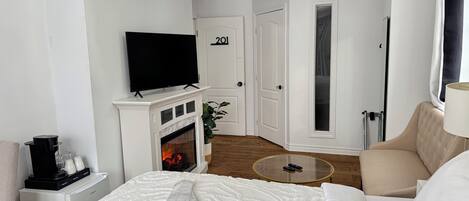 A hotel room with a bed, a TV mounted above a fireplace, a door labeled "201", and a round glass table.