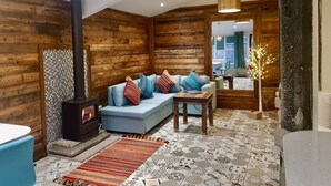 A cozy log cabin interior with a sofa, a small table, a fireplace, and a decorative tree. - Lymestone Boutique Accommodation (Grange-over-Sands)