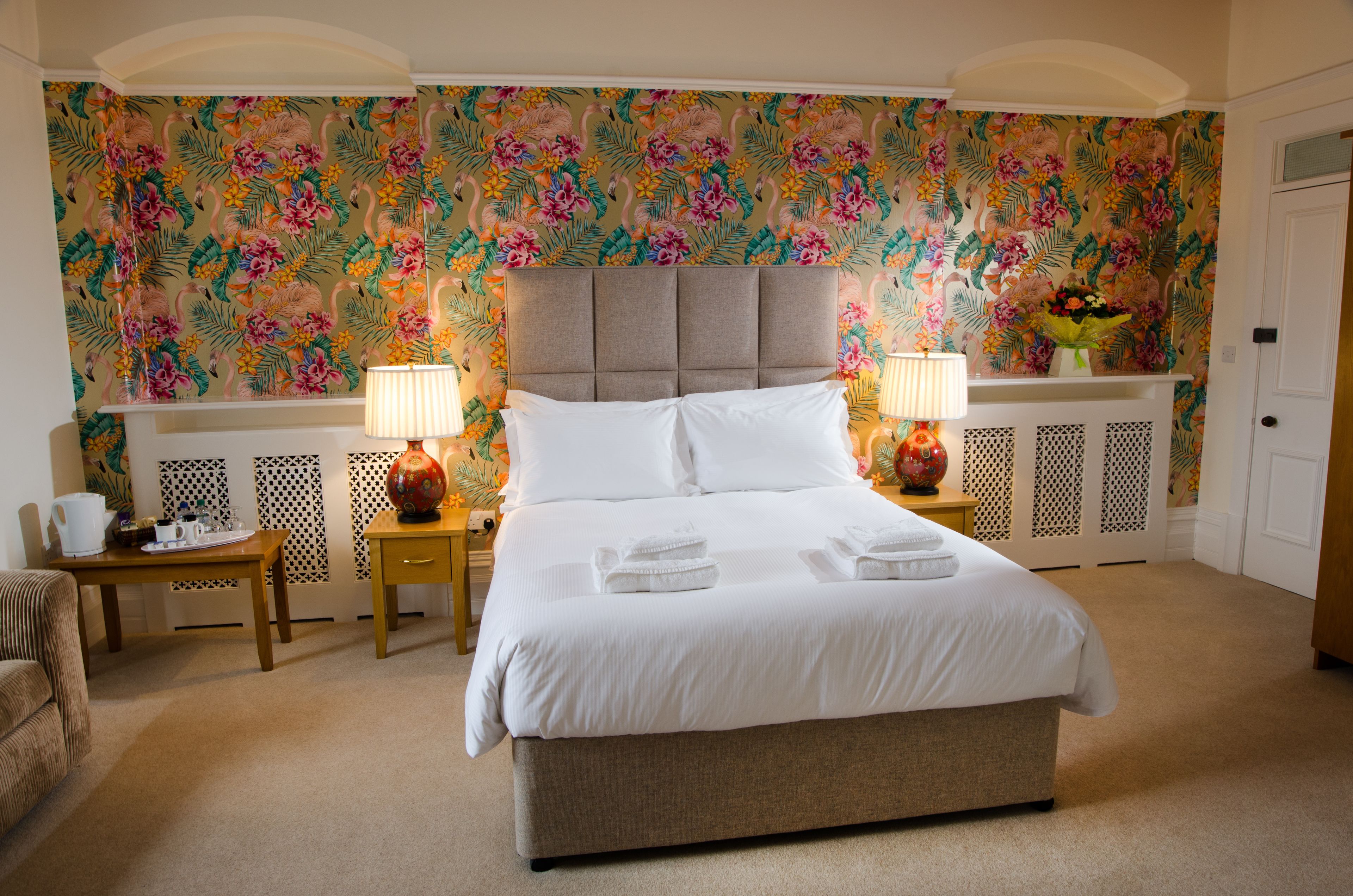 A neatly made bed with white linens, two bedside lamps, and a floral wallpaper.