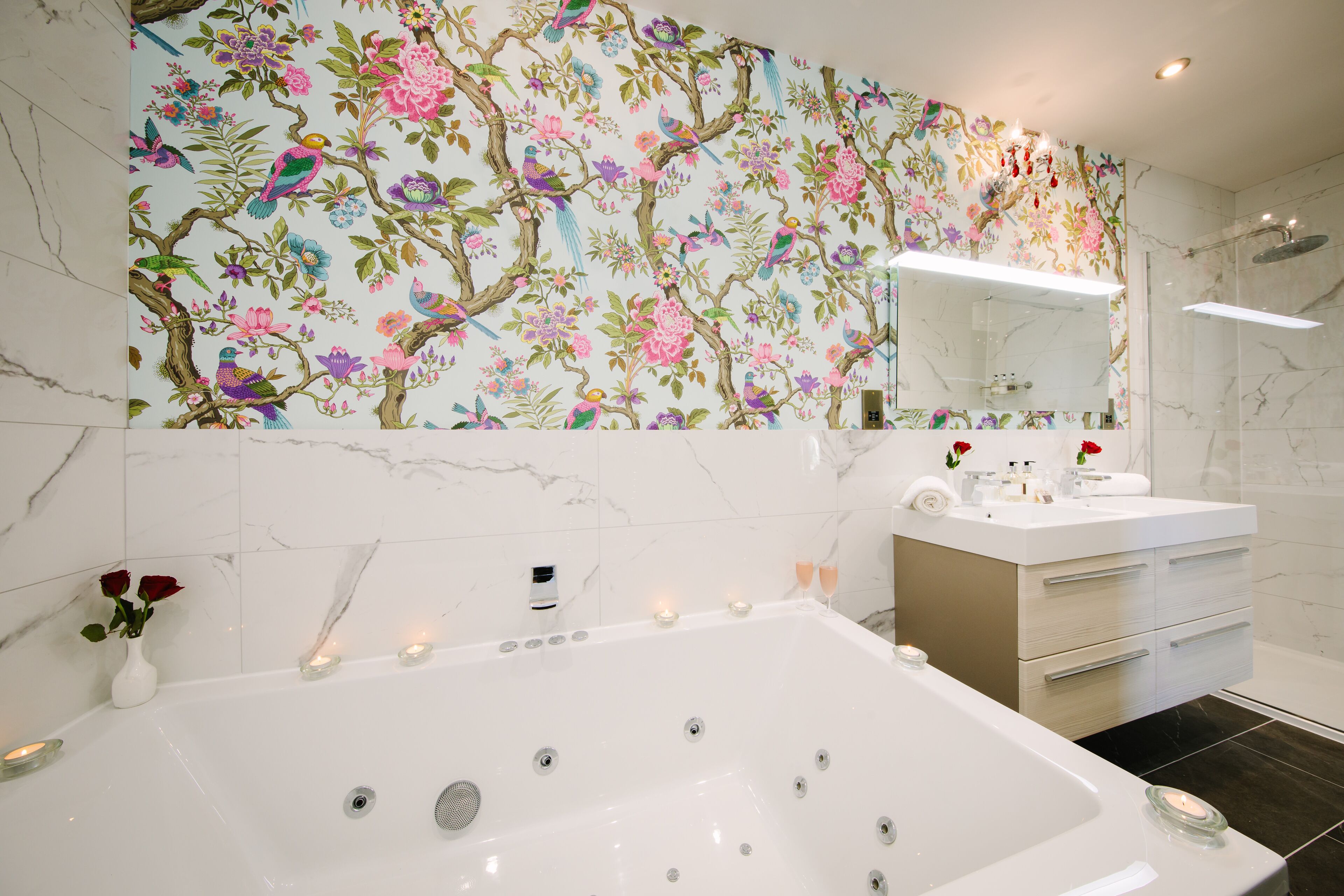 A modern bathroom with a large bathtub, a vanity with a mirror, and a floral wallpaper design.