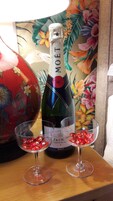 Una botella de Moët & Chandon, dos copas con adornos rojos y un jarrón decorativo sobre una mesa de madera.