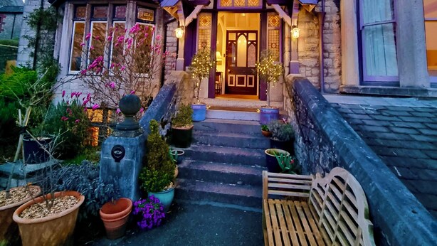 A stone building with a traditional architectural style, featuring a prominent entrance with a decorative door and windows. - Lymestone Boutique Accommodation (Grange-over-Sands)