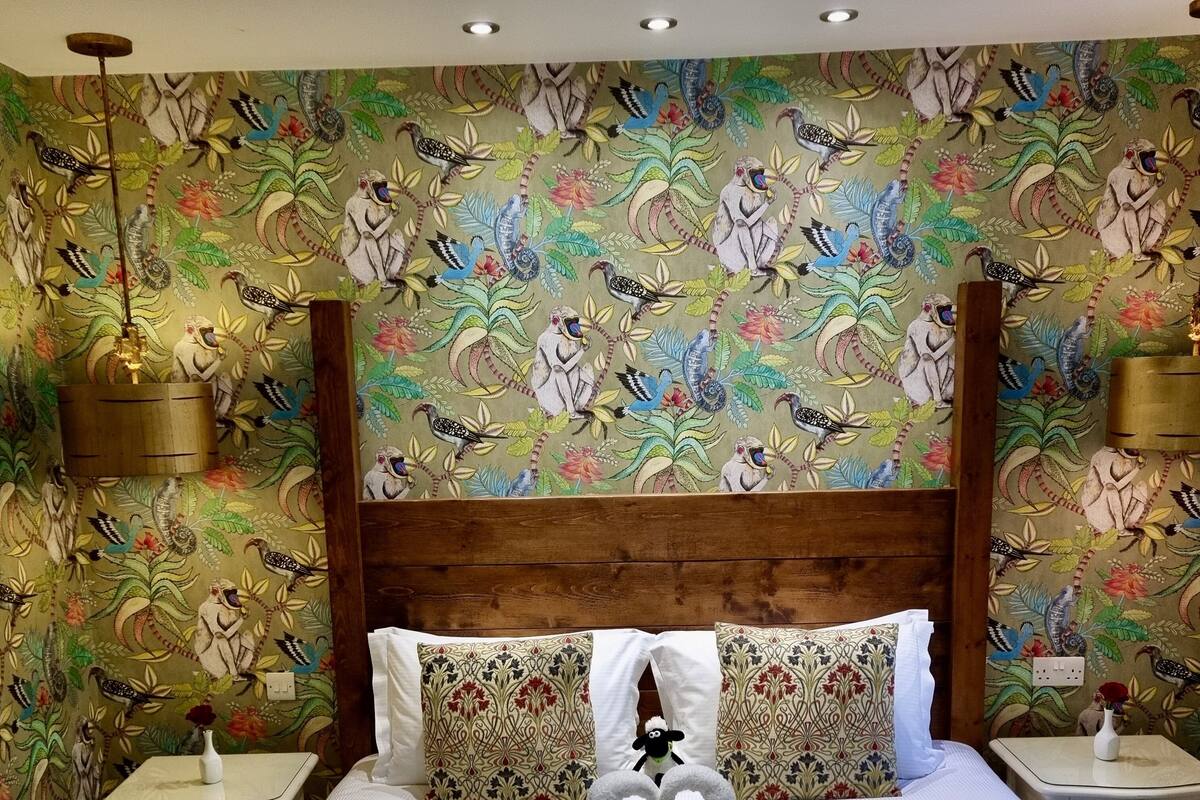 Une chambre d’hôtel avec un grand lit, un papier peint à motifs floraux et une serviette pliée en forme de cœur.